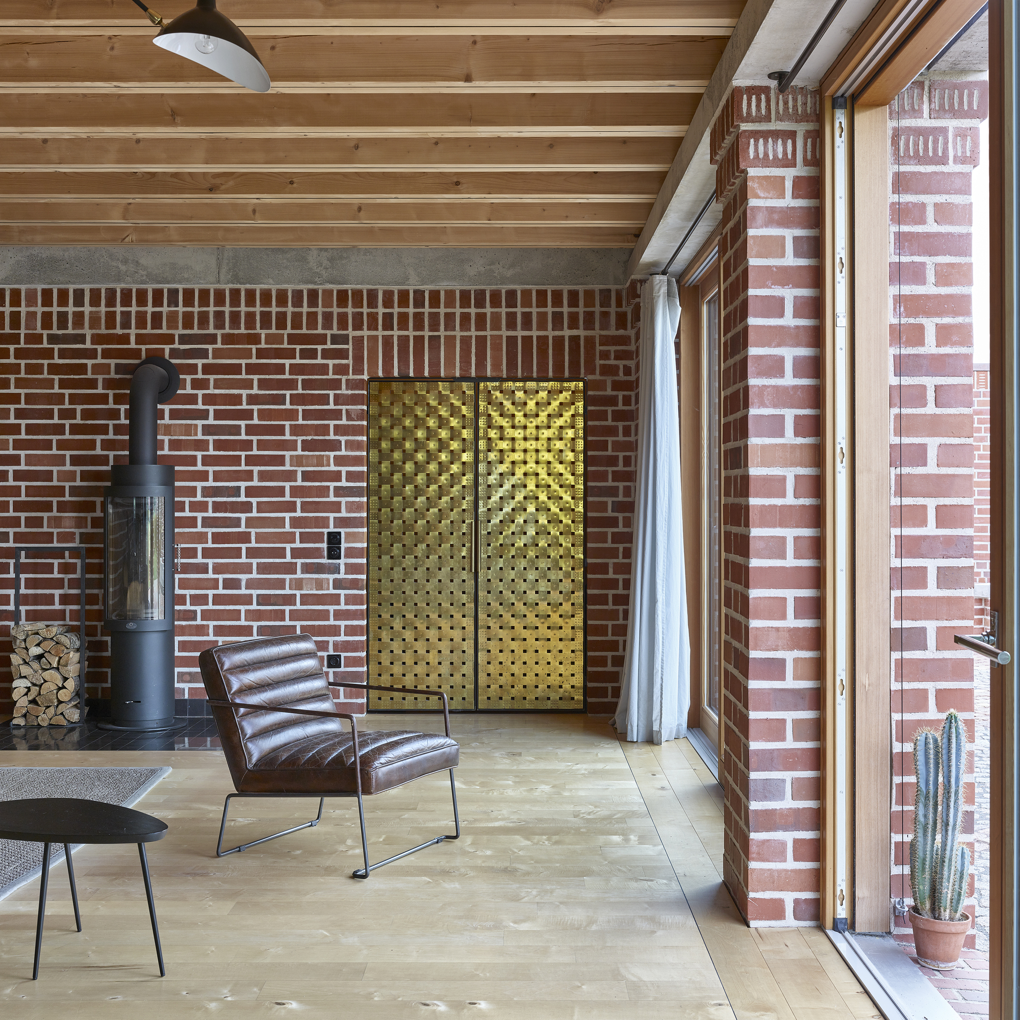 Interior living space with exposed timber ceiling, red brick walls, brass textured panels and leather chair