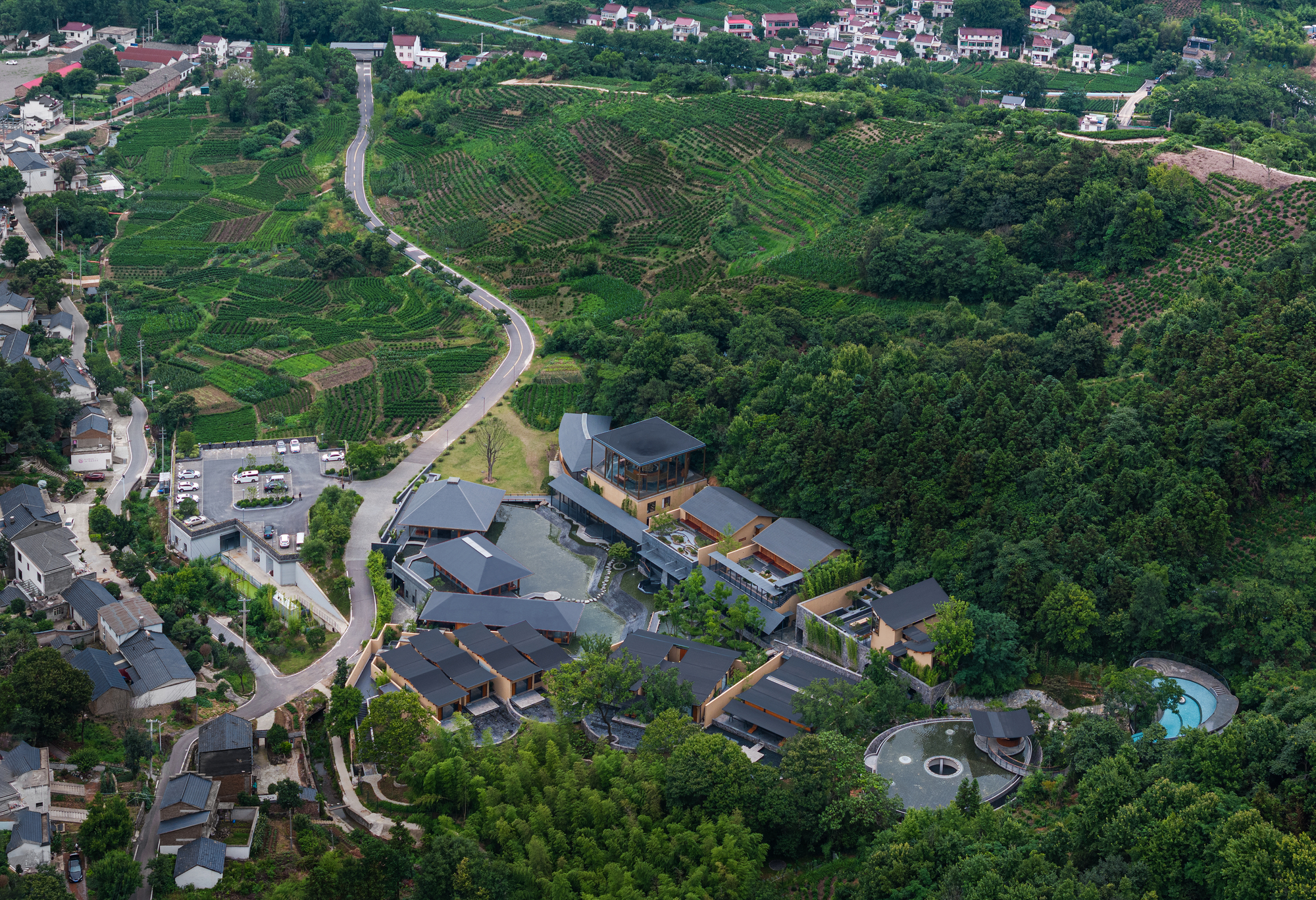 Drone view of the compound nestled between agricultural terraces and wooded slopes in daylight
