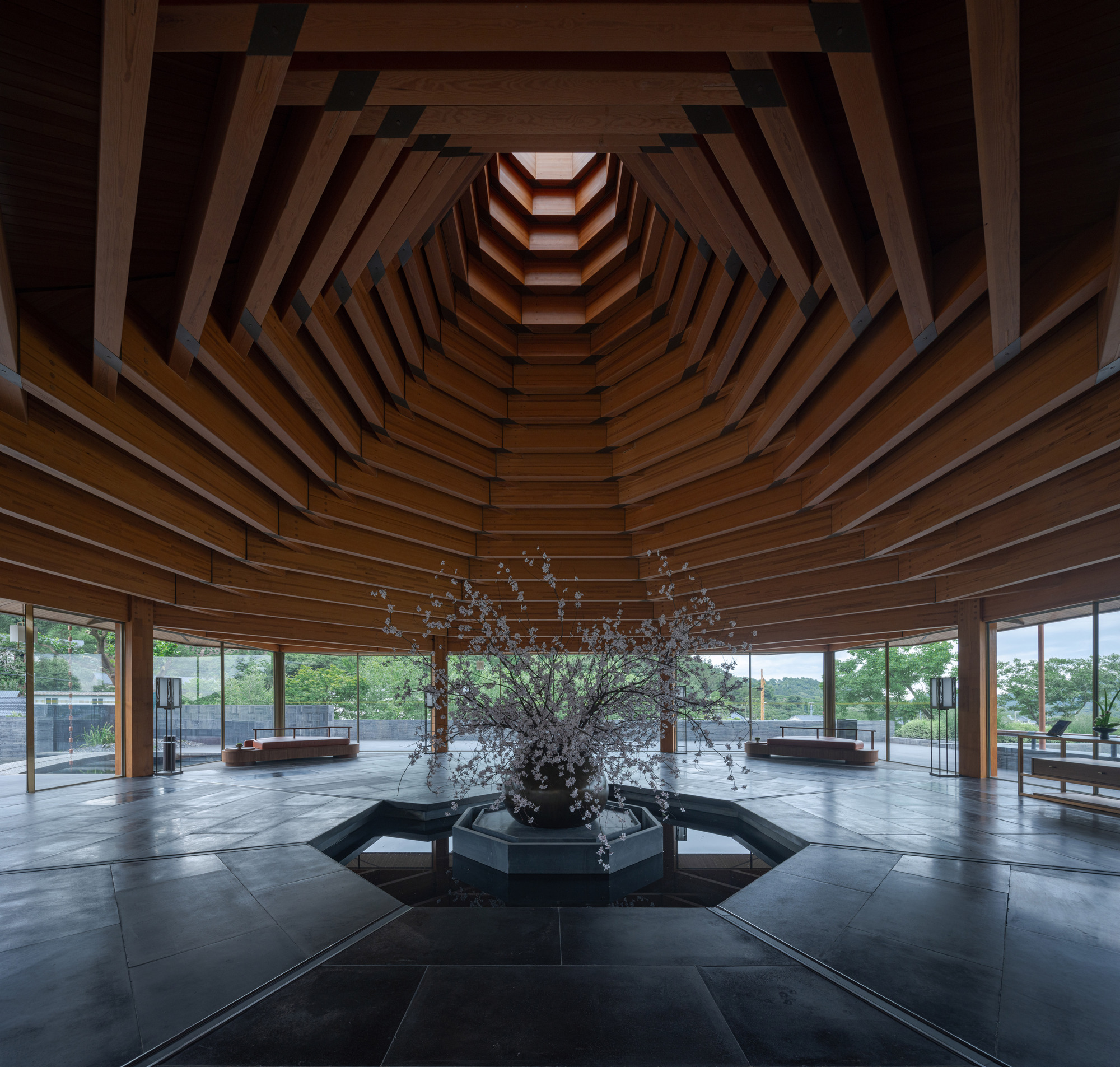 Stepped timber ceiling coffers radiating upward around a central skylight above a sculptural branch arrangement