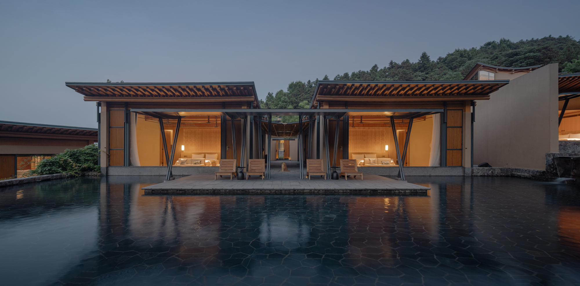 Twin pavilions with exposed timber roofs flanking a reflecting pool at dusk