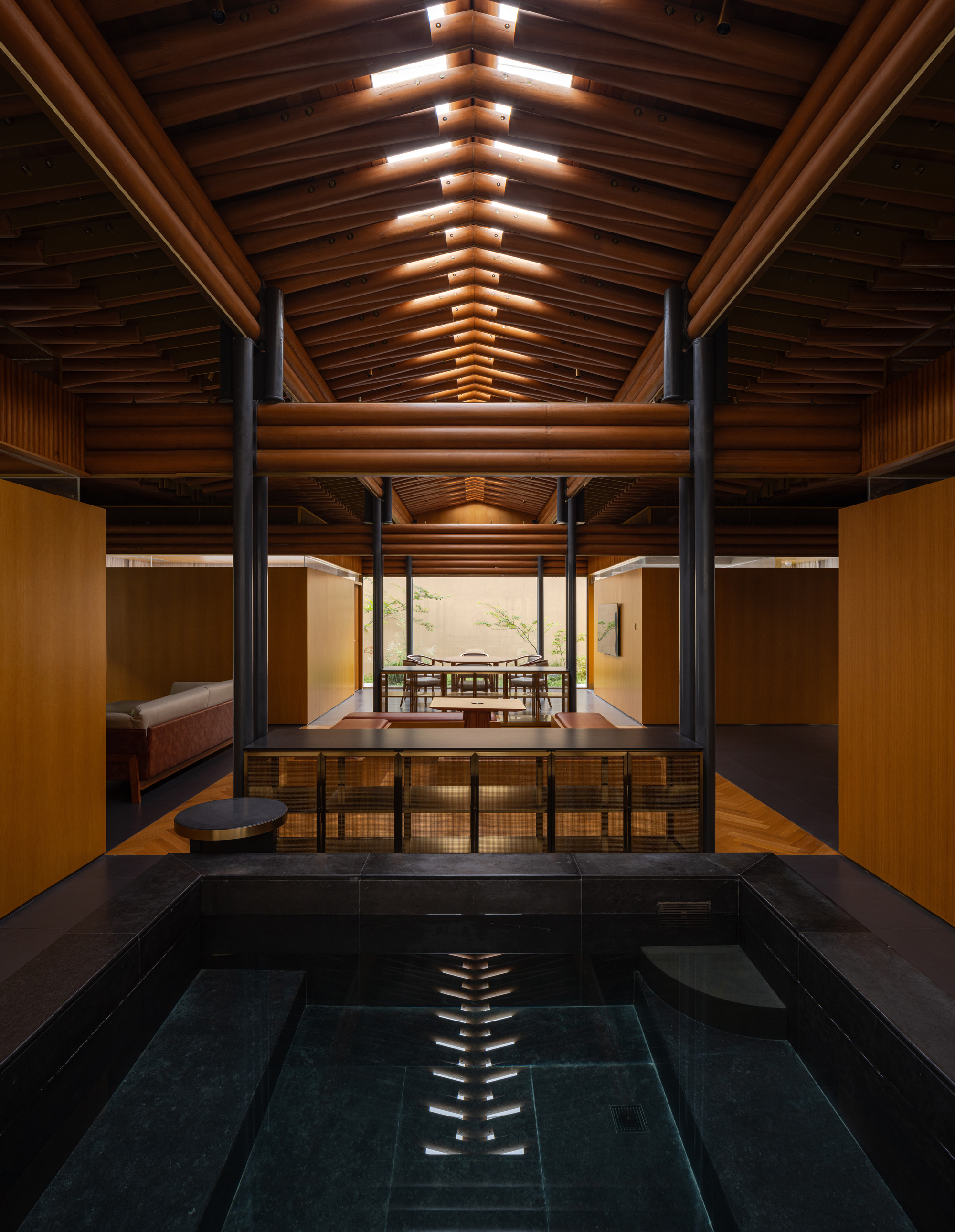 Indoor bath with dark tile surround beneath a vaulted timber ceiling with steel bracing