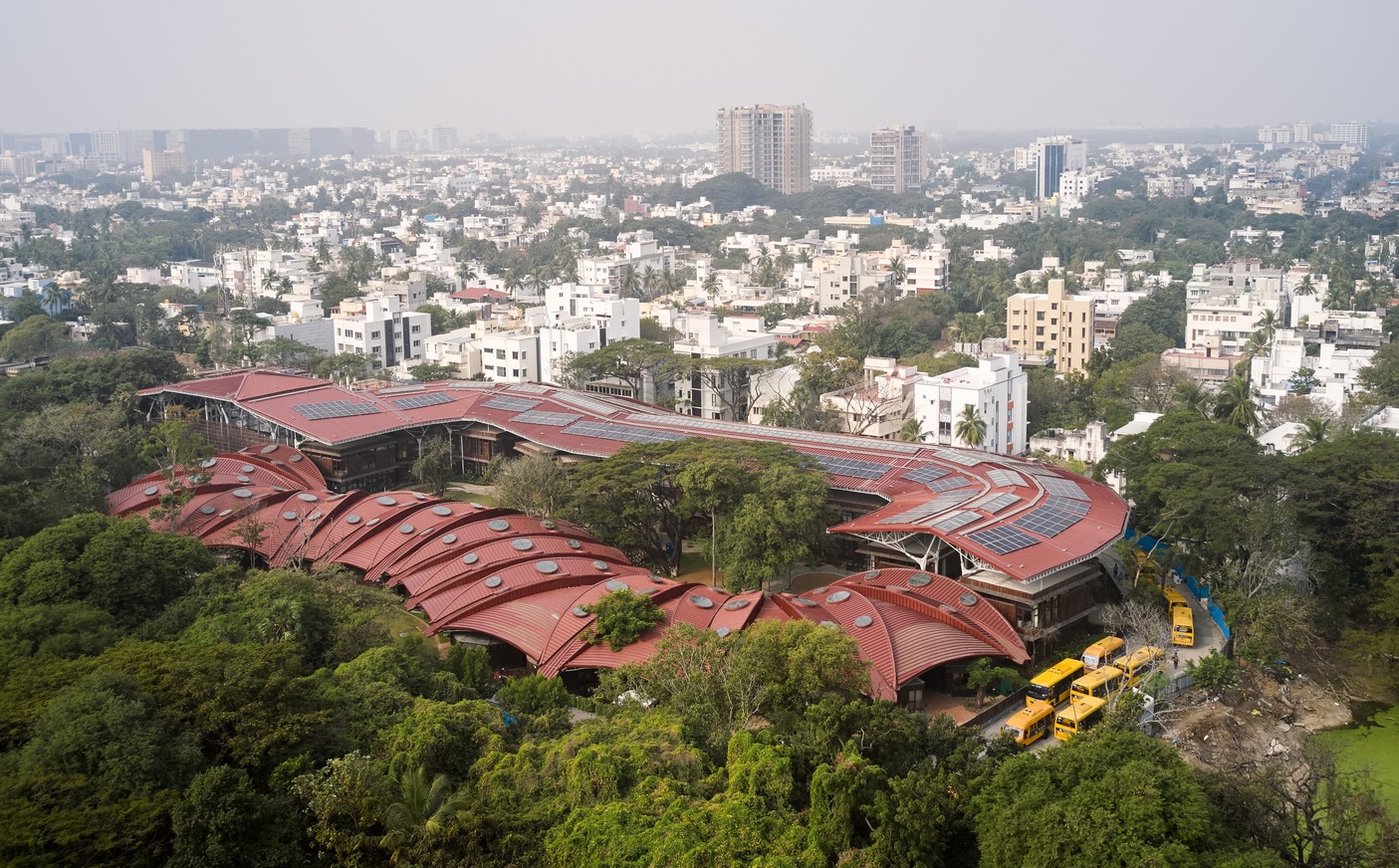 Aerial view of the undulating terracotta metal roof with solar panels overlooking a dense urban neighborhood