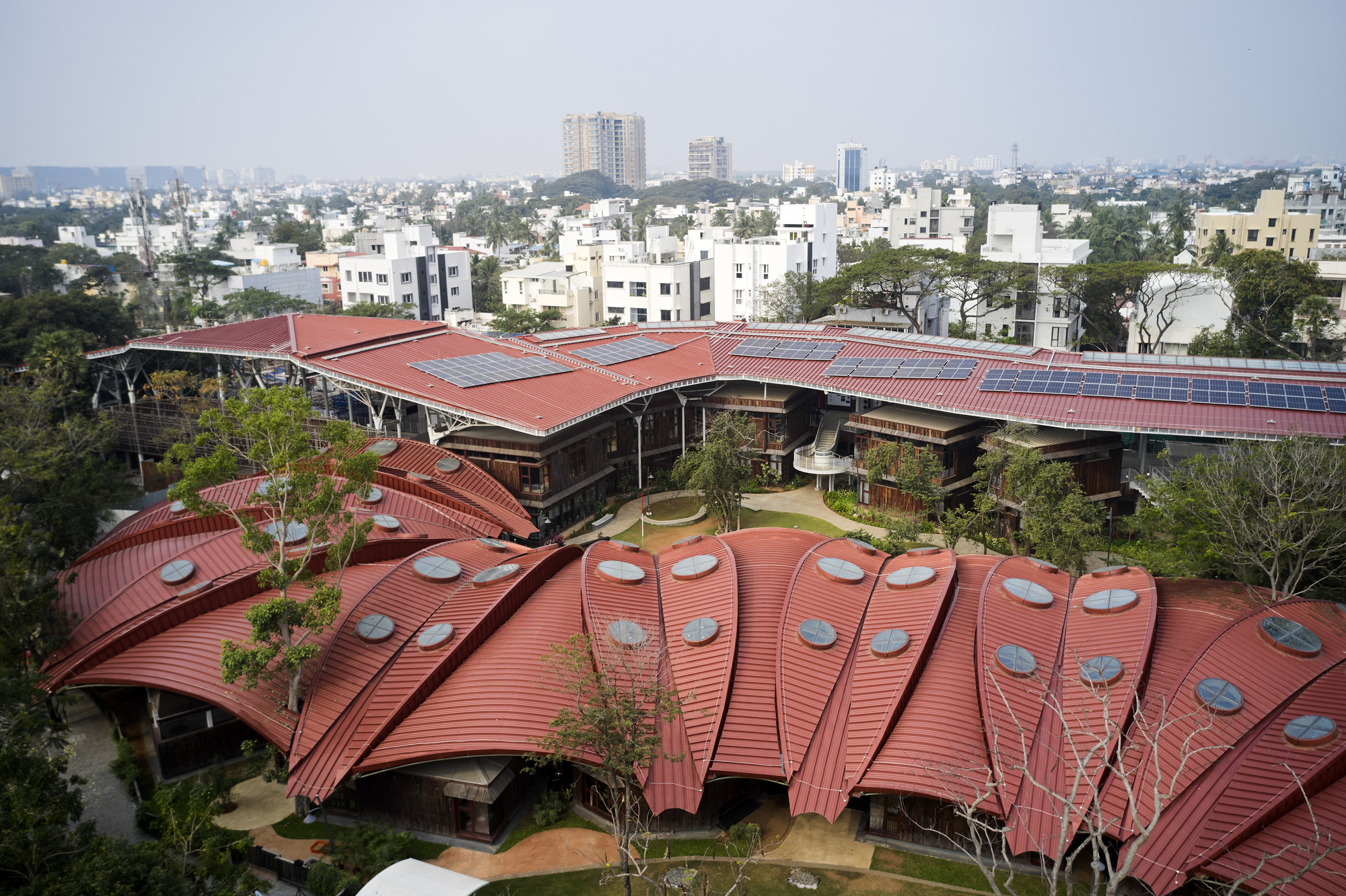 The ribbed metal roof with circular skylights extending over a central courtyard with trees and pathways