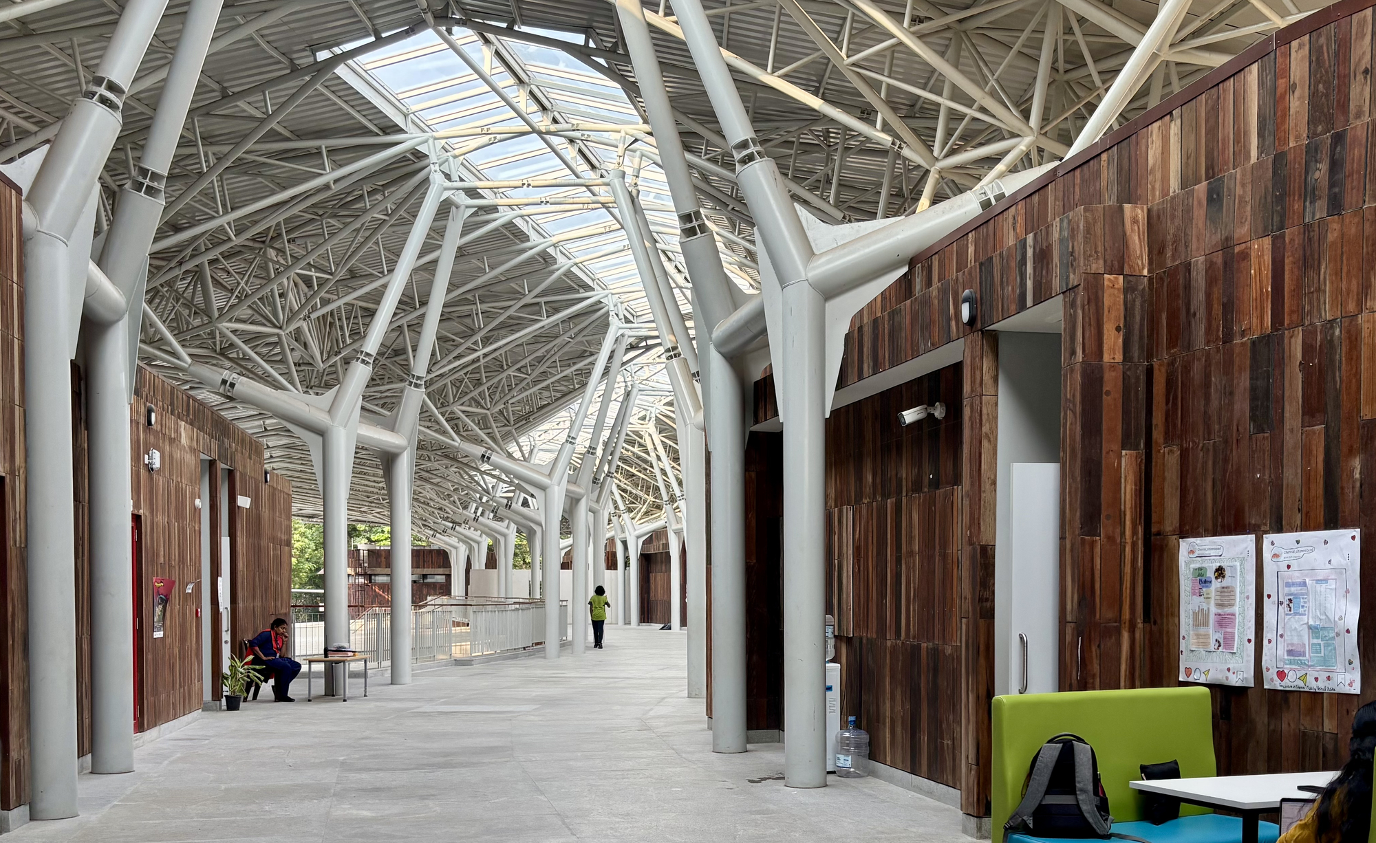 Interior corridor with white steel space frame overhead and timber-clad volumes with a person seated