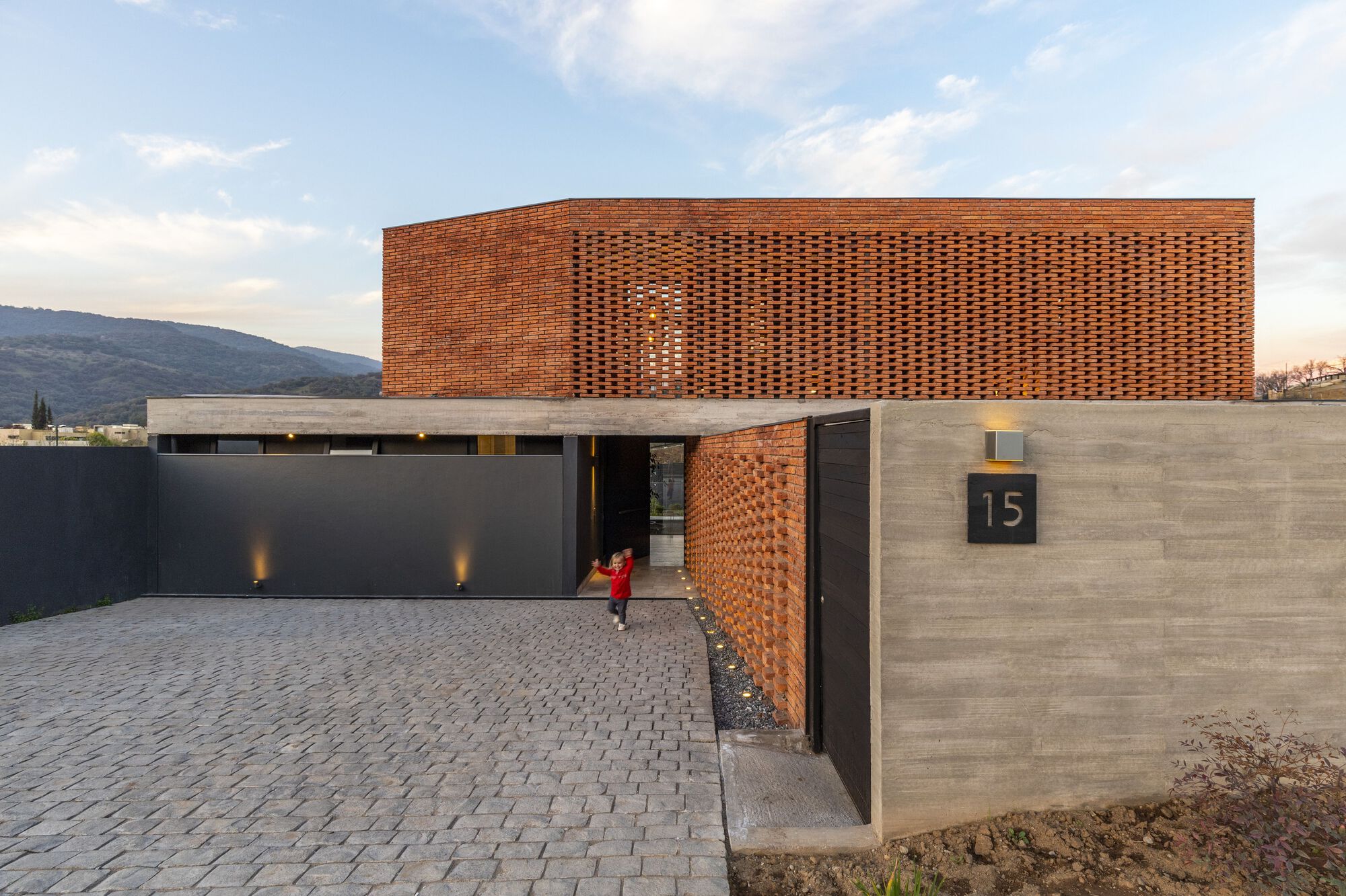 Entry courtyard with perforated brick volume above concrete base and child in red crossing the paving