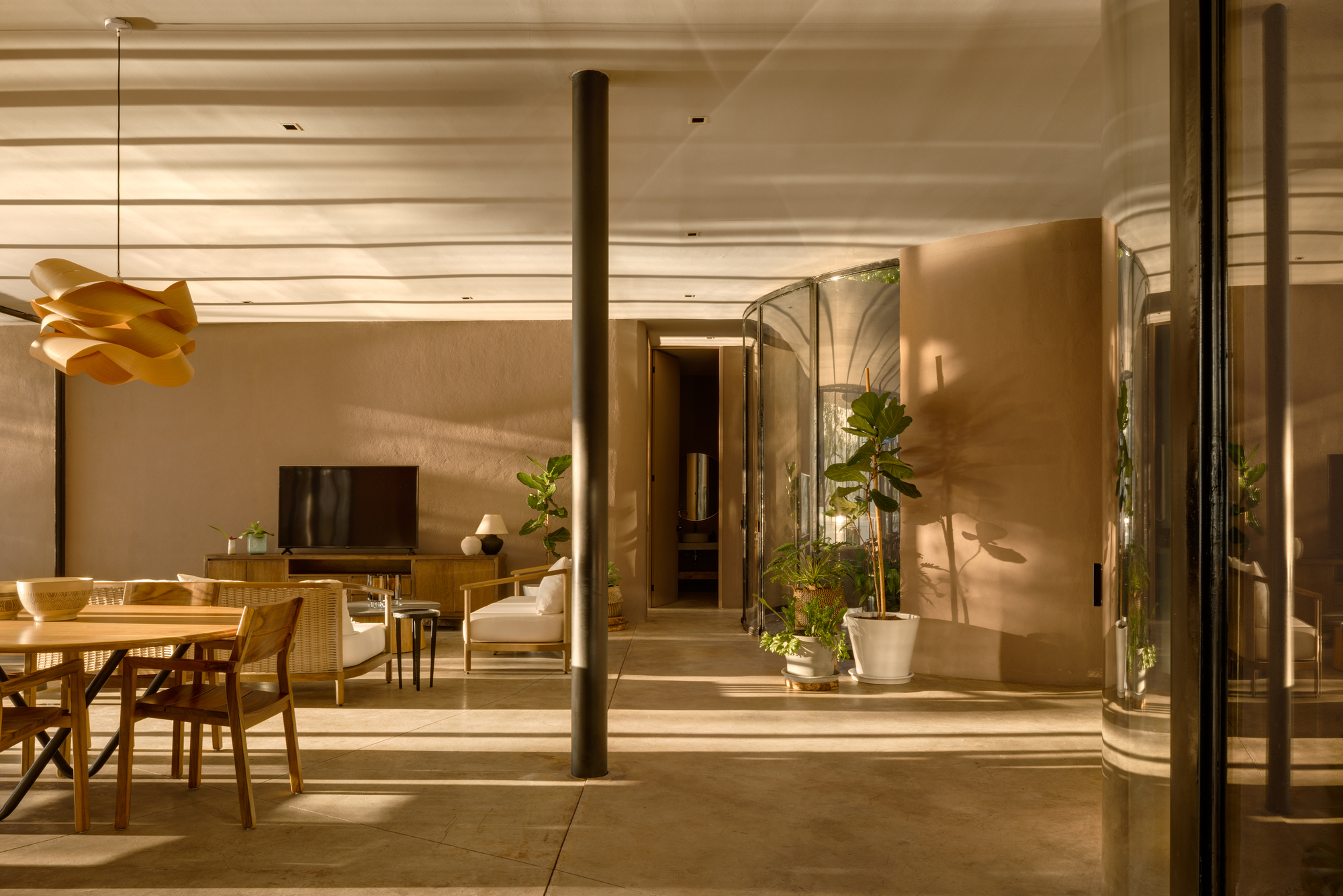Open-plan living and dining space with concrete floors and curved plaster walls lit by evening light