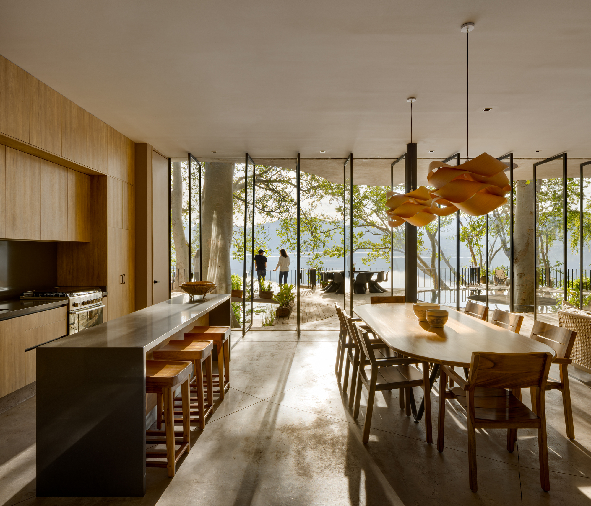 Kitchen and dining area with island, timber cabinetry, and floor-to-ceiling glass opening to the terrace