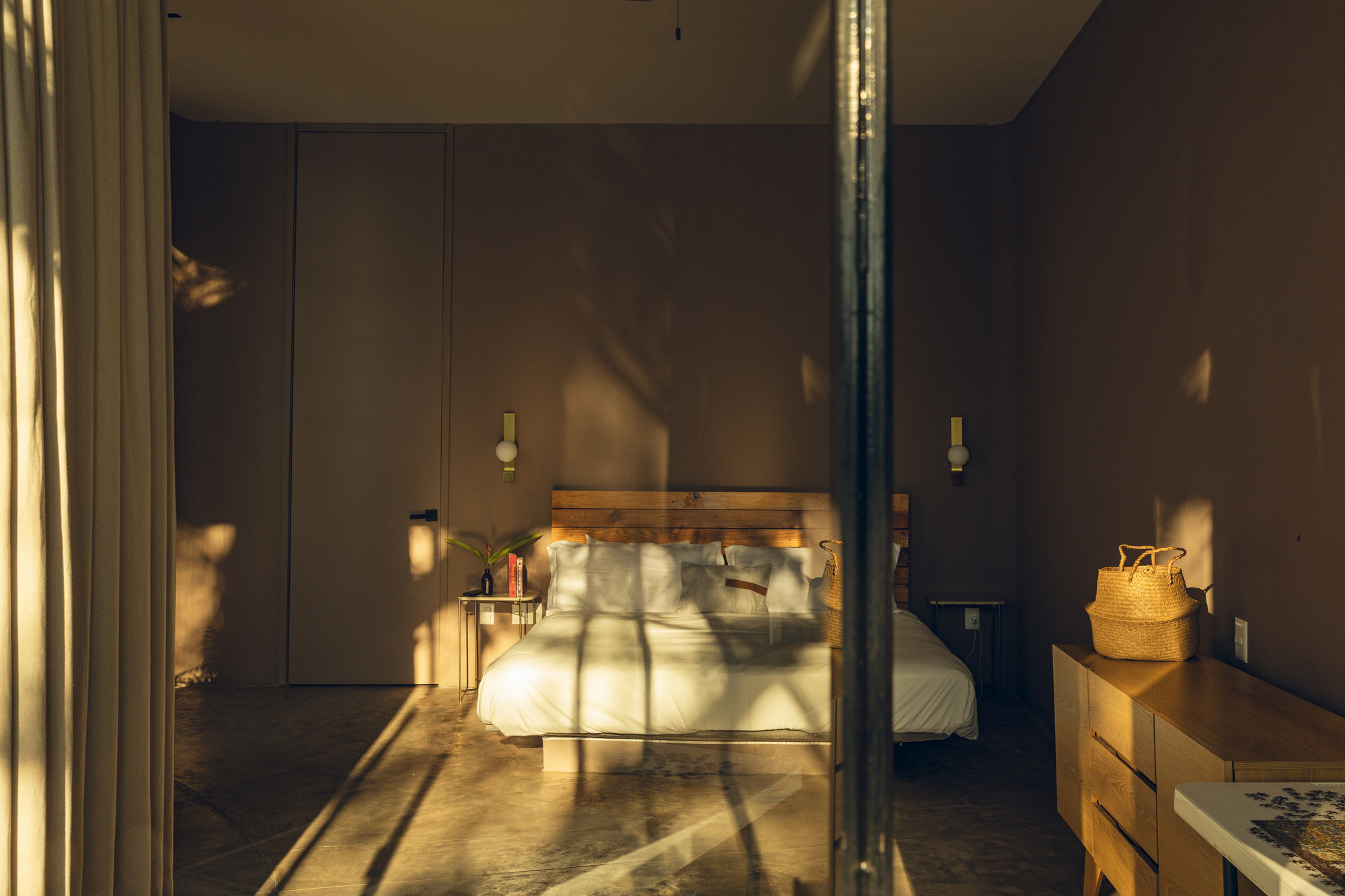 Bedroom interior with sunlight and tree shadows projected onto the grey wall behind the bed