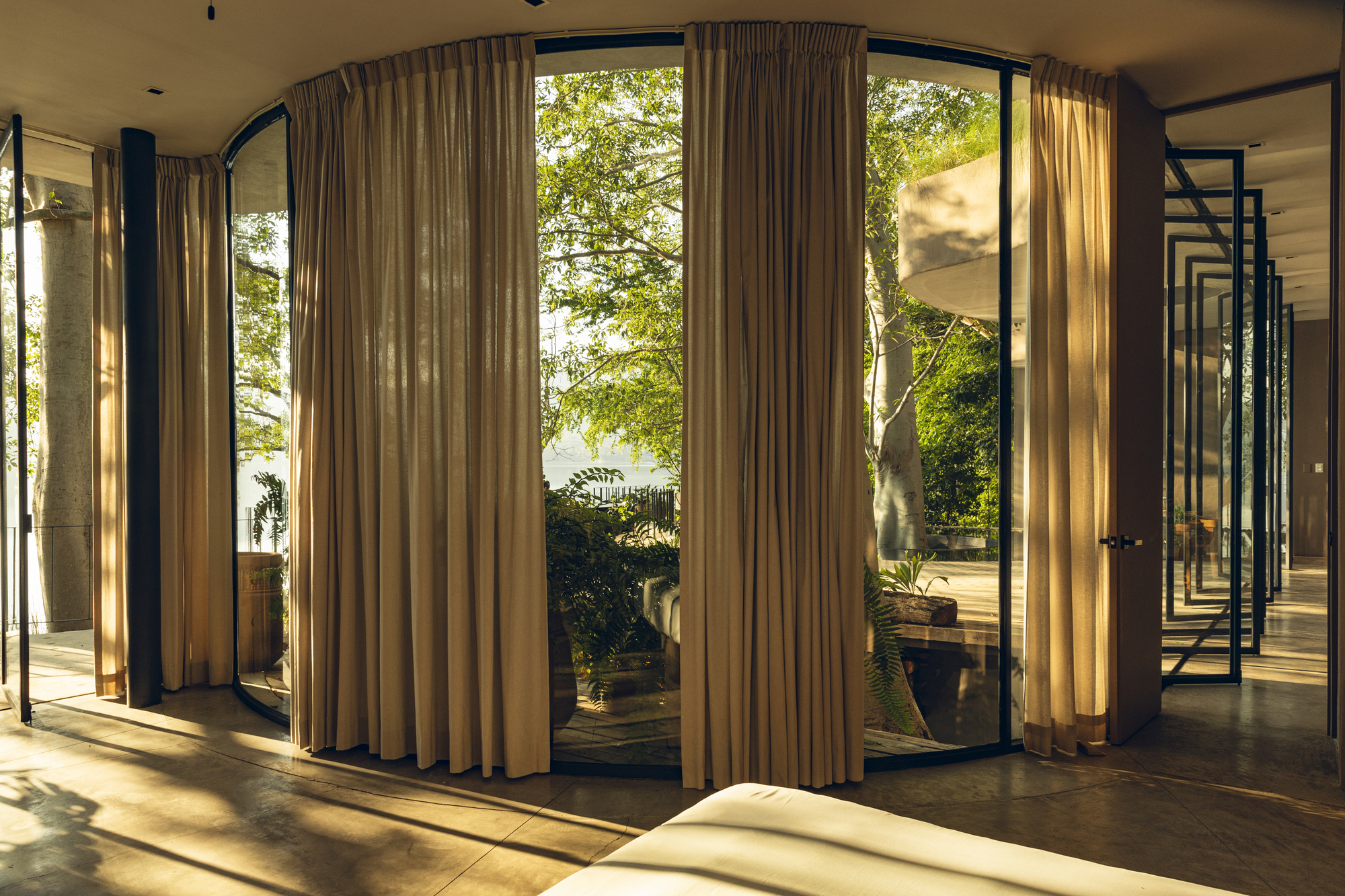 Floor-to-ceiling curtains framing glazed doors that open to a planted terrace in afternoon light