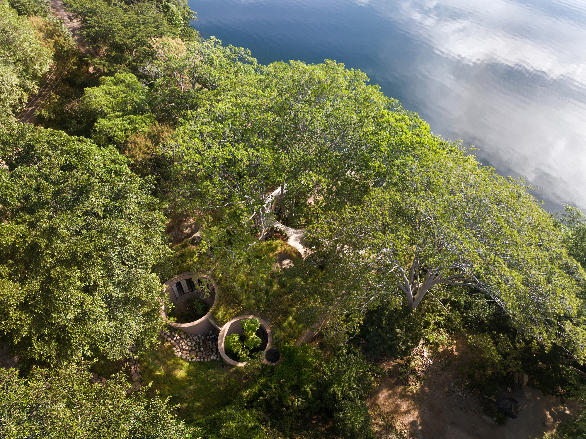 Aerial view of the curved roof structures nestled among dense tree canopy and open waterfront