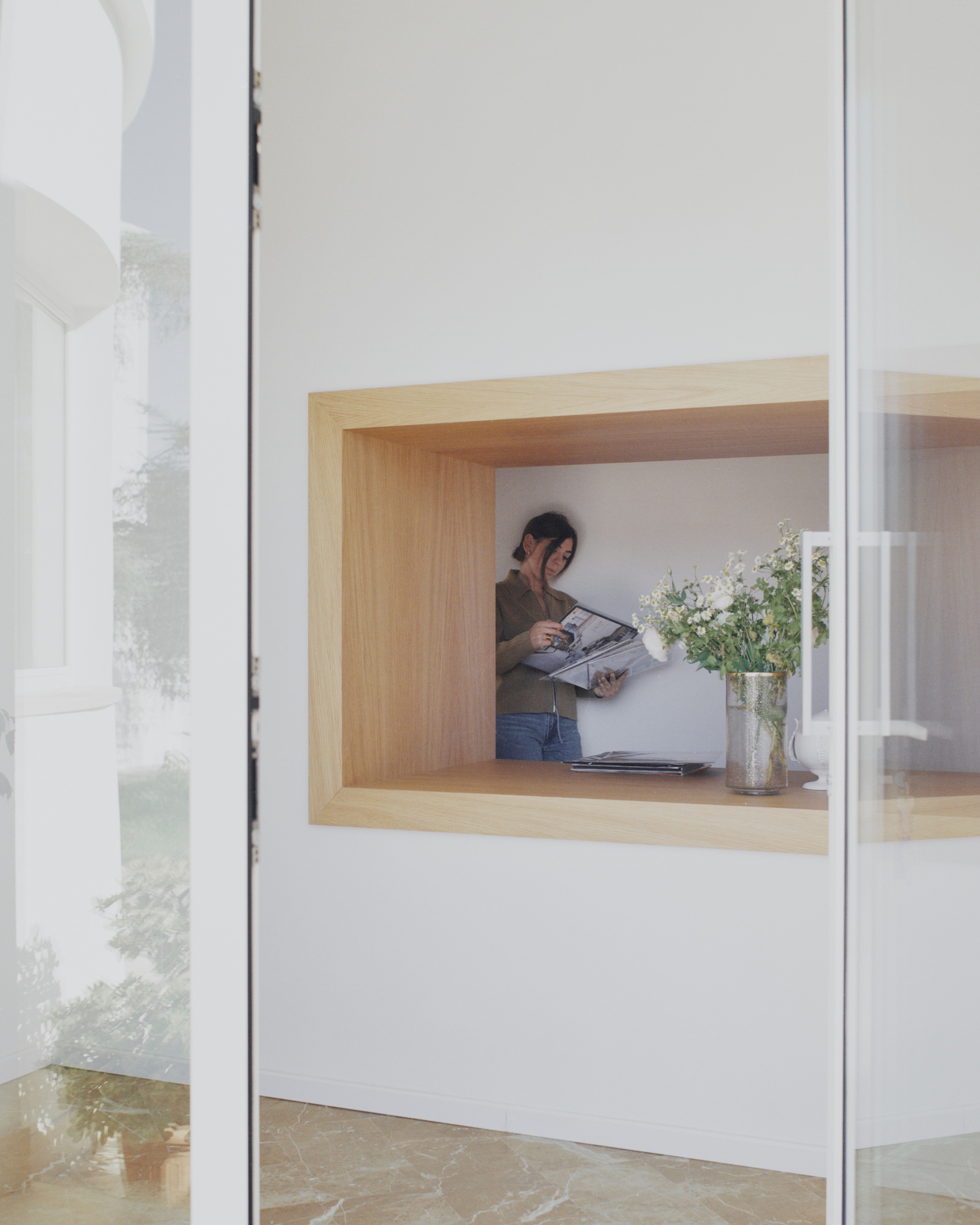 Timber-lined window nook with a person reading while standing beside a vase of flowers