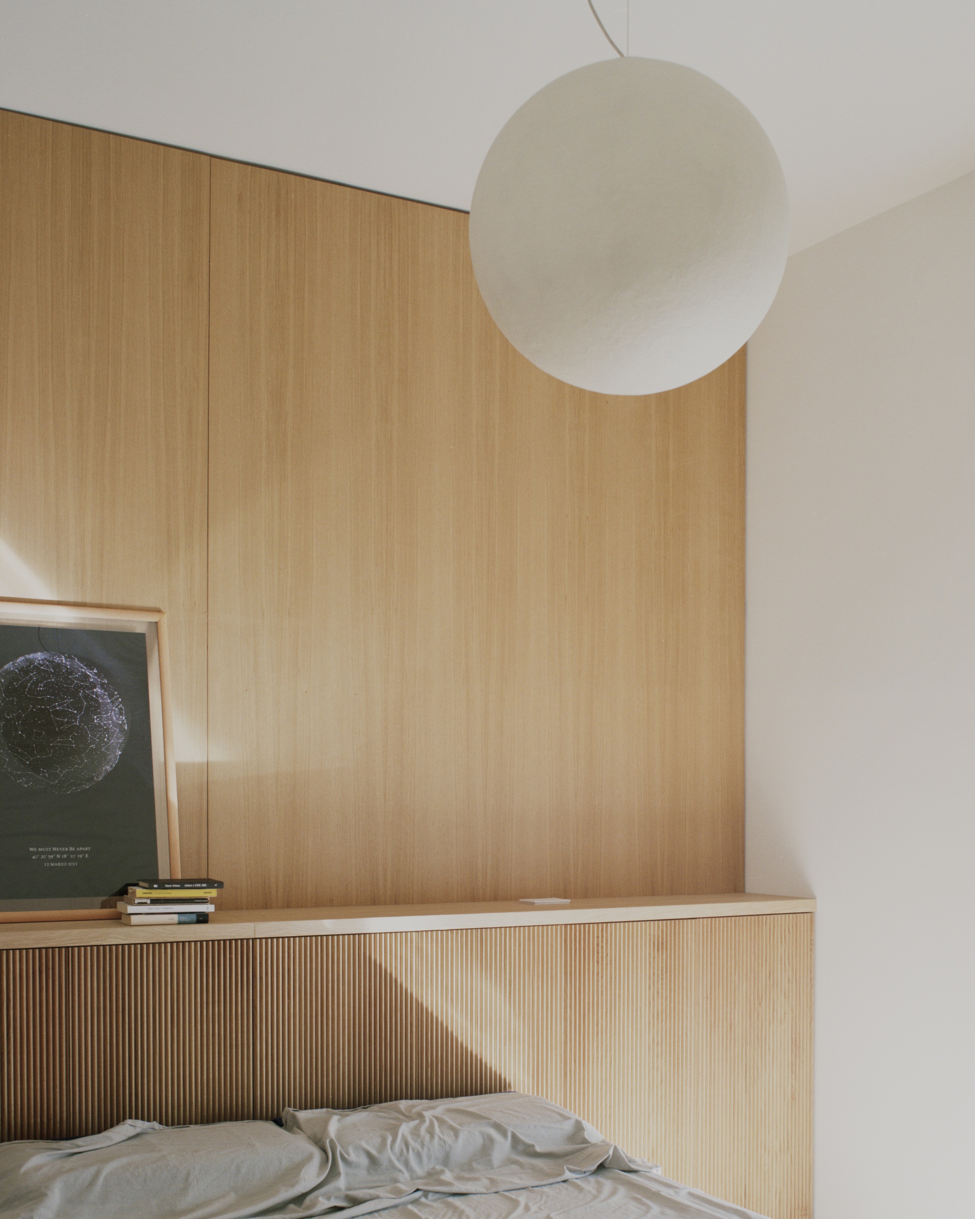 Bedroom corner with ribbed oak headboard wall and spherical pendant light above the bed