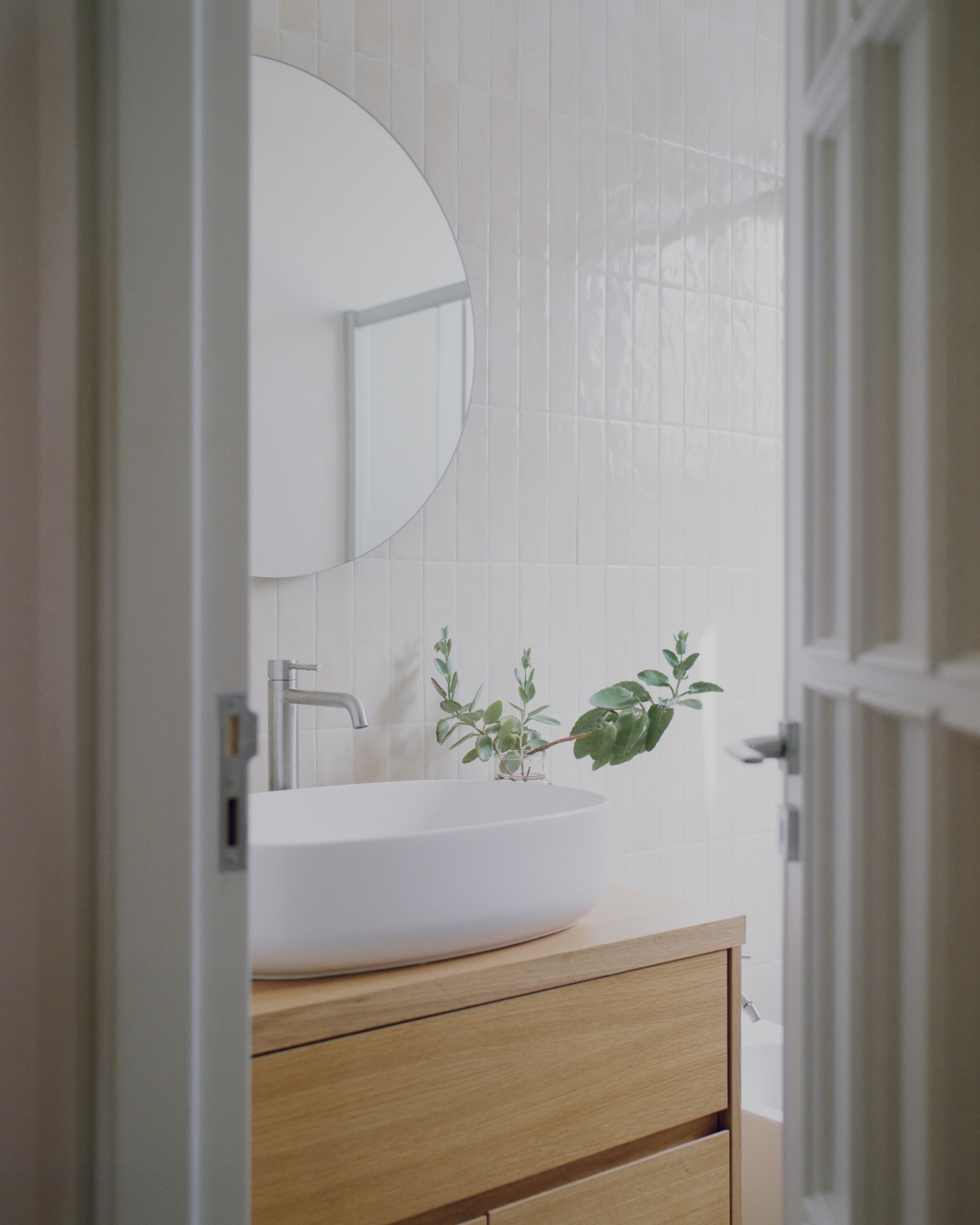 Bathroom vanity with vessel sink on oak cabinetry beneath vertical white tiles and a round mirror