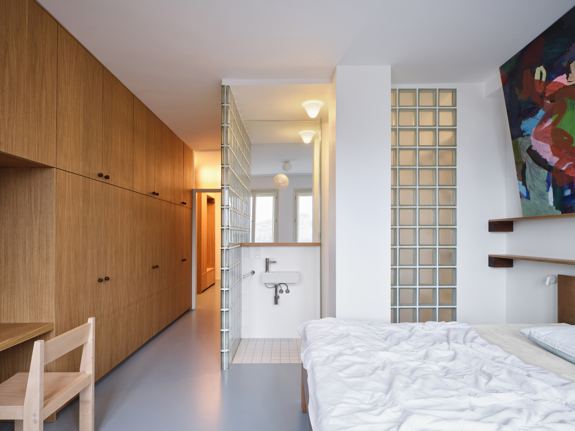 Bedroom with glass block privacy wall, built-in oak cabinetry and ensuite bathroom beyond