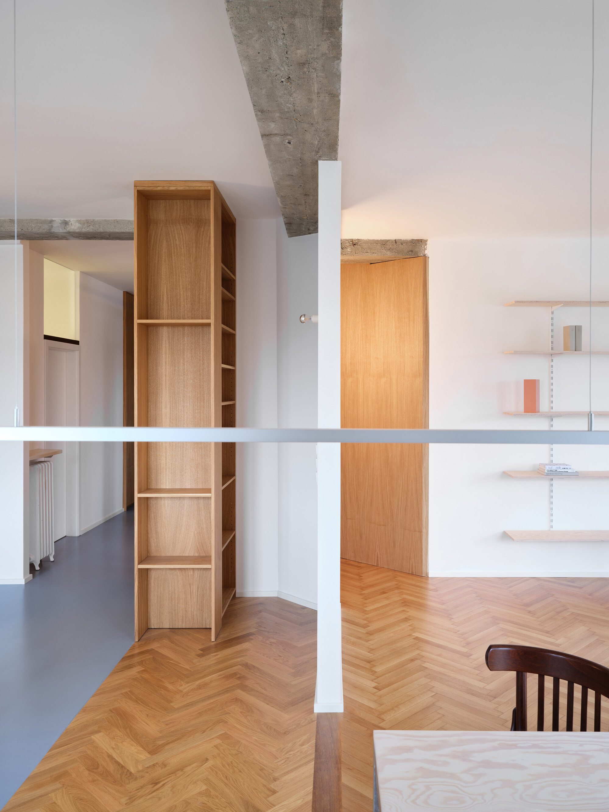 View across white horizontal rail showing oak bookshelf unit and exposed concrete beam above