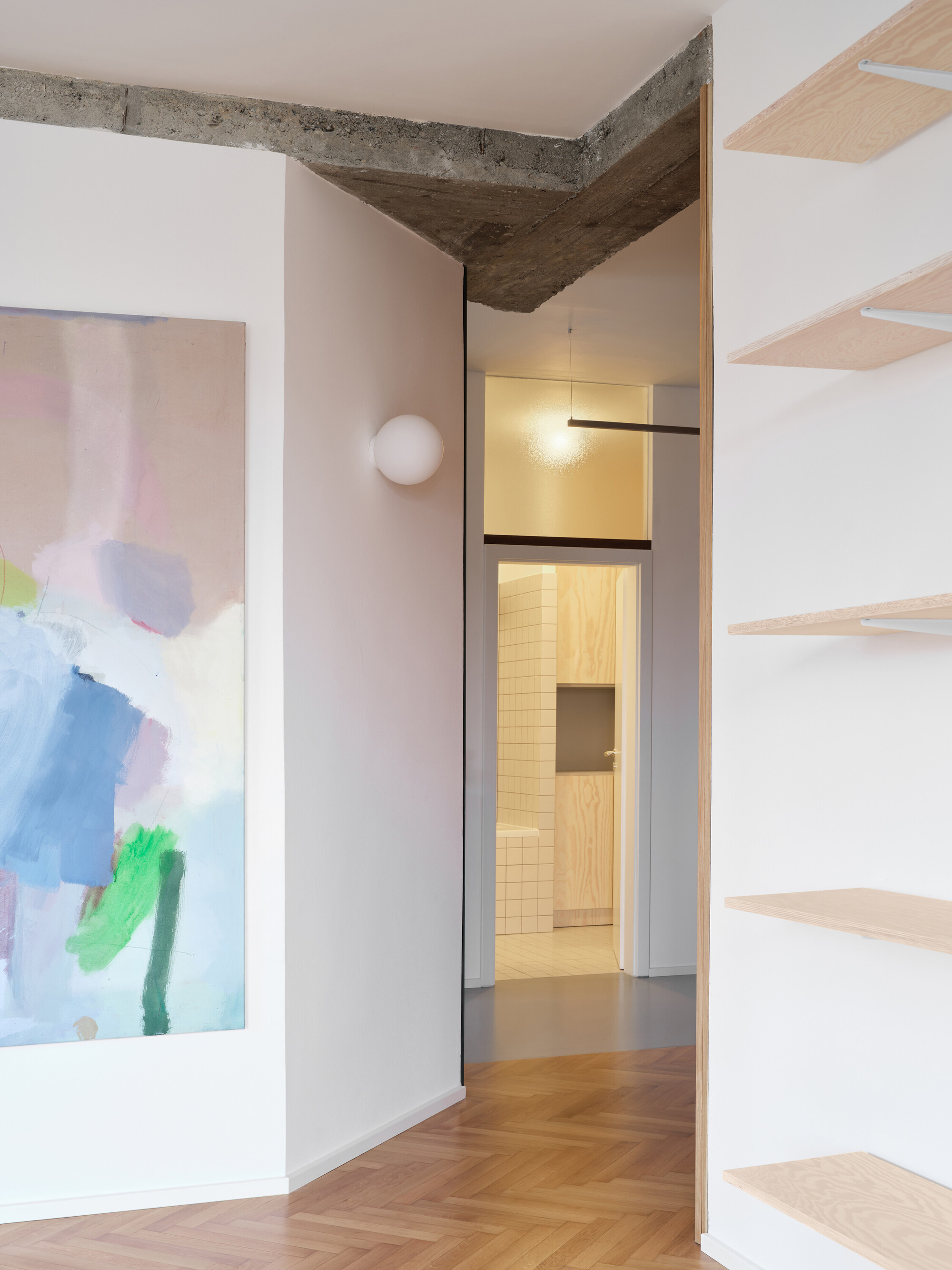 Interior hallway with exposed concrete ceiling beam and herringbone wood floor leading to a tiled room