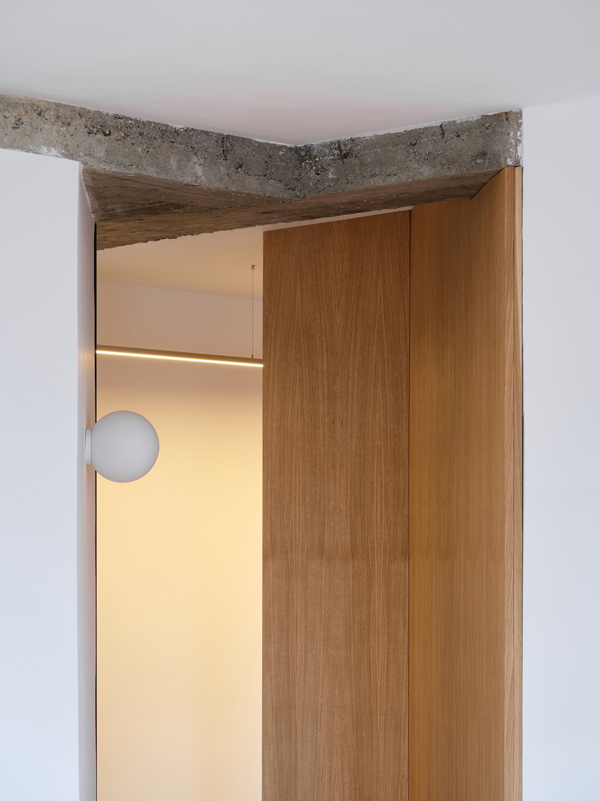 Doorway detail showing exposed concrete lintel above timber door frame with globe light visible beyond