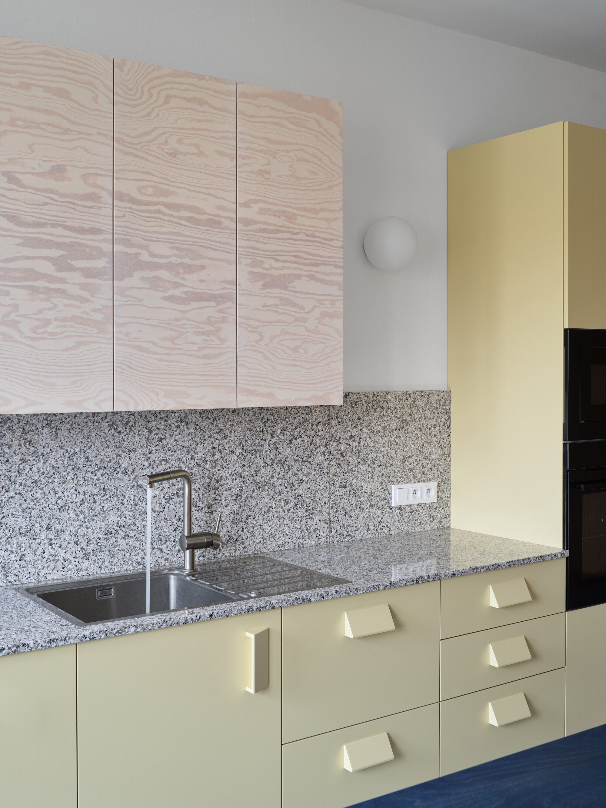Kitchen counter with terrazzo backsplash, pale yellow lower cabinets and whitewashed plywood uppers