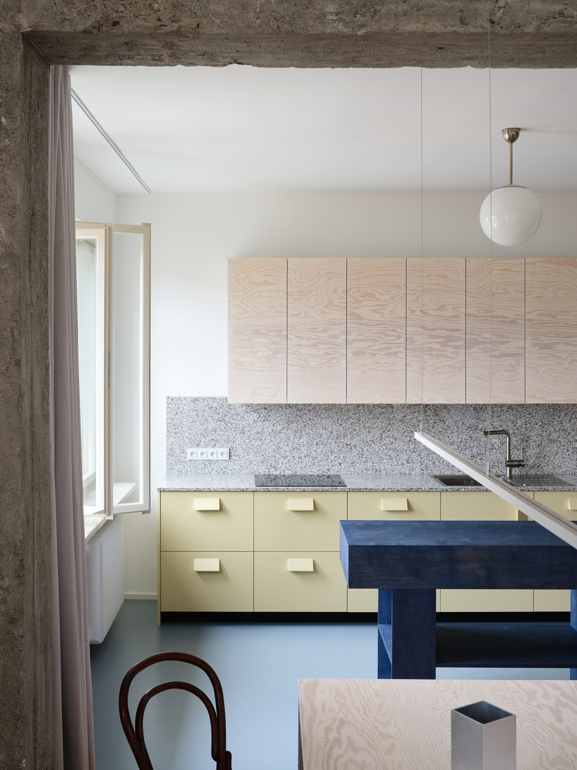 Kitchen view through concrete doorway with blue bench, yellow cabinets and hanging globe pendant
