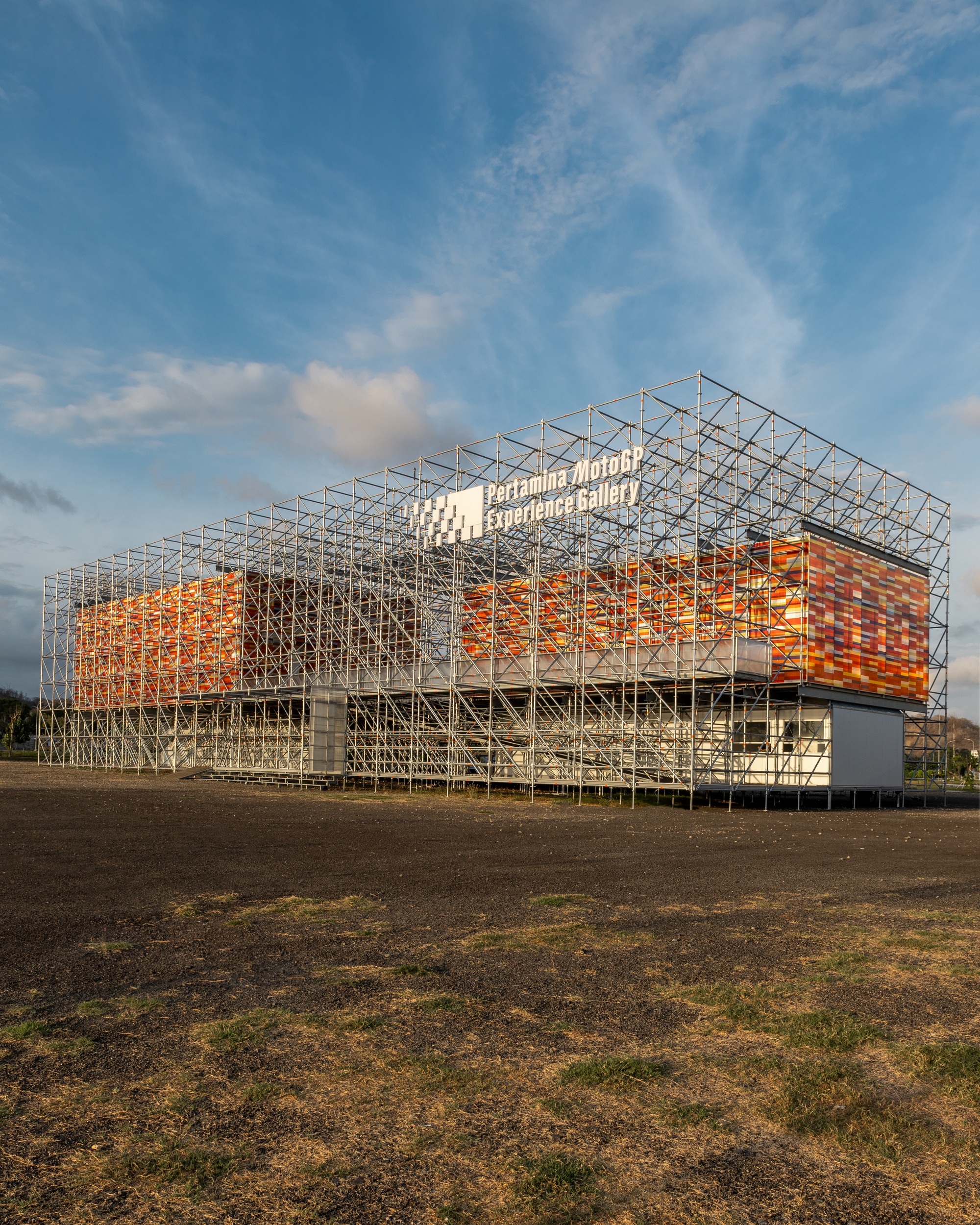 Corner perspective of the steel frame pavilion with woven orange facade under evening clouds