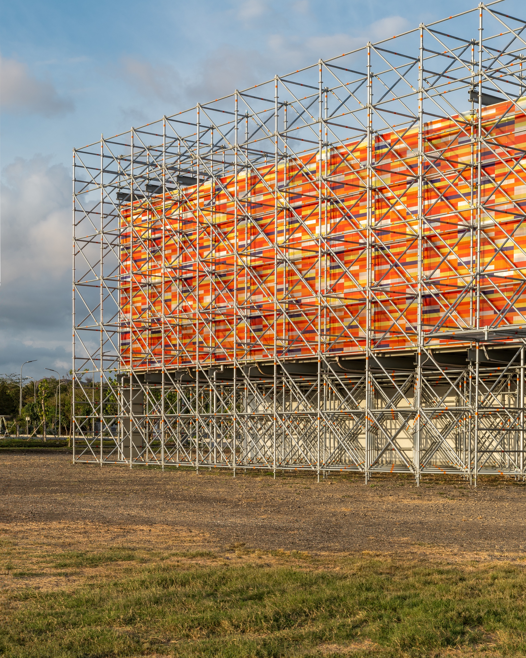 Close-up of the diagonal steel truss members supporting the orange woven panel screen