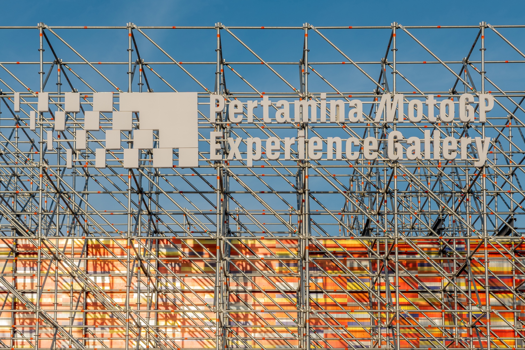 Close view of steel truss framework above the colored panel screen against clear blue sky