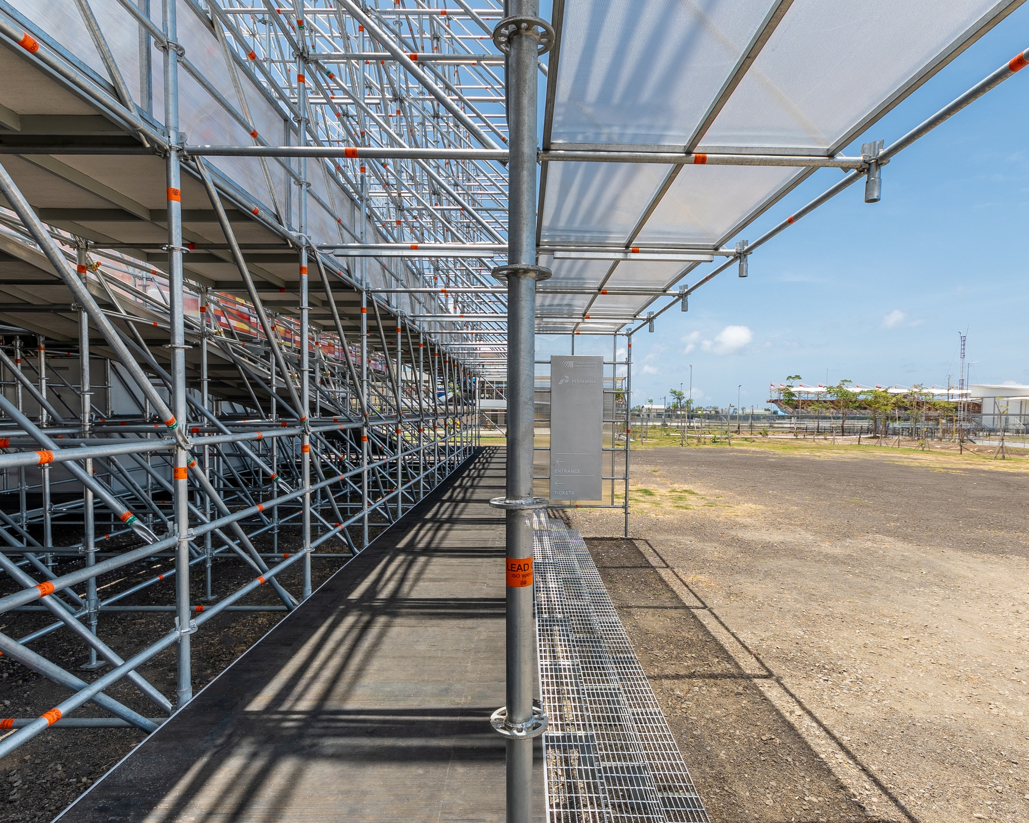 Covered walkway with steel scaffolding columns and translucent canopy panels under midday sun