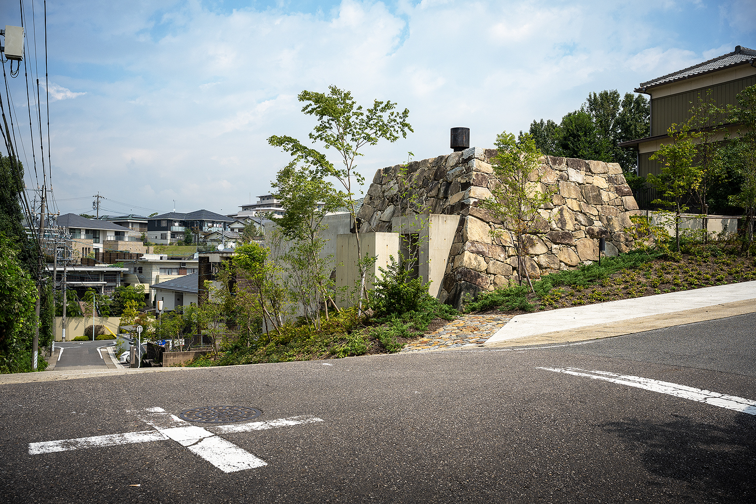 Street view of the boulder-like stone structure atop a graded hillside with young trees
