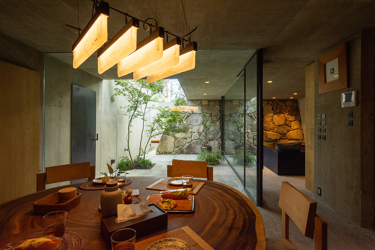 Interior dining area with suspended timber light fixture overlooking a courtyard garden through glass walls
