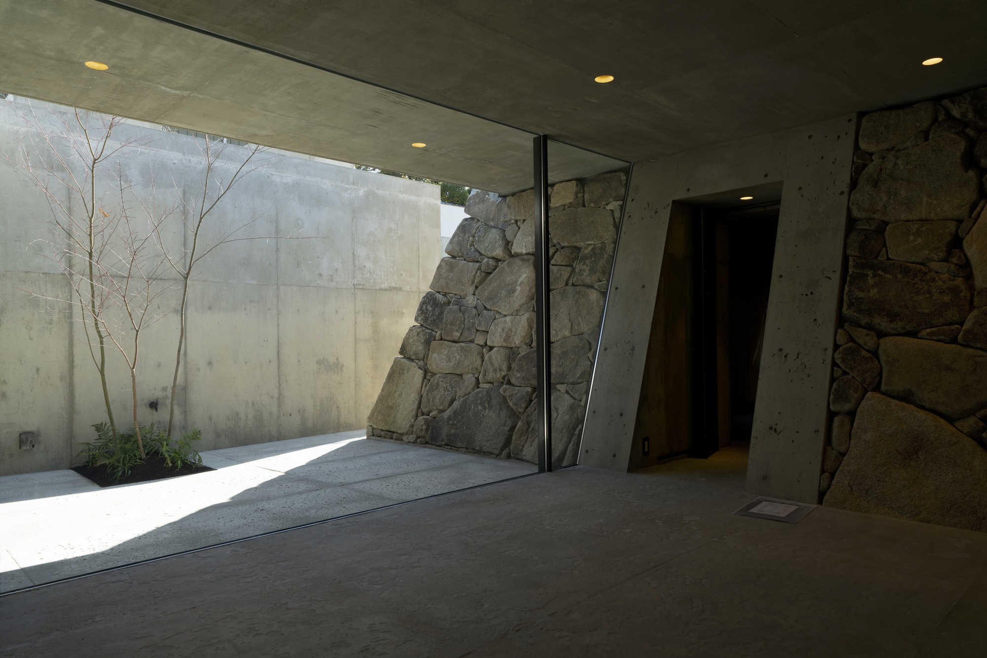 Corner view of the glass-walled courtyard showing the angled stone mass and planted bed