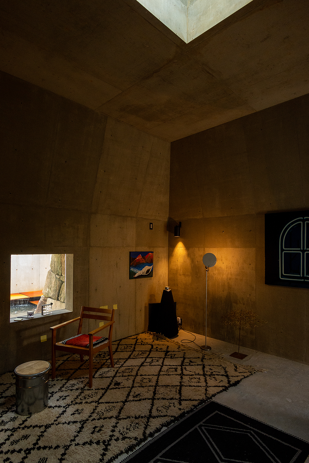 Plywood-lined living room with a corner skylight and framed window overlooking an exterior courtyard