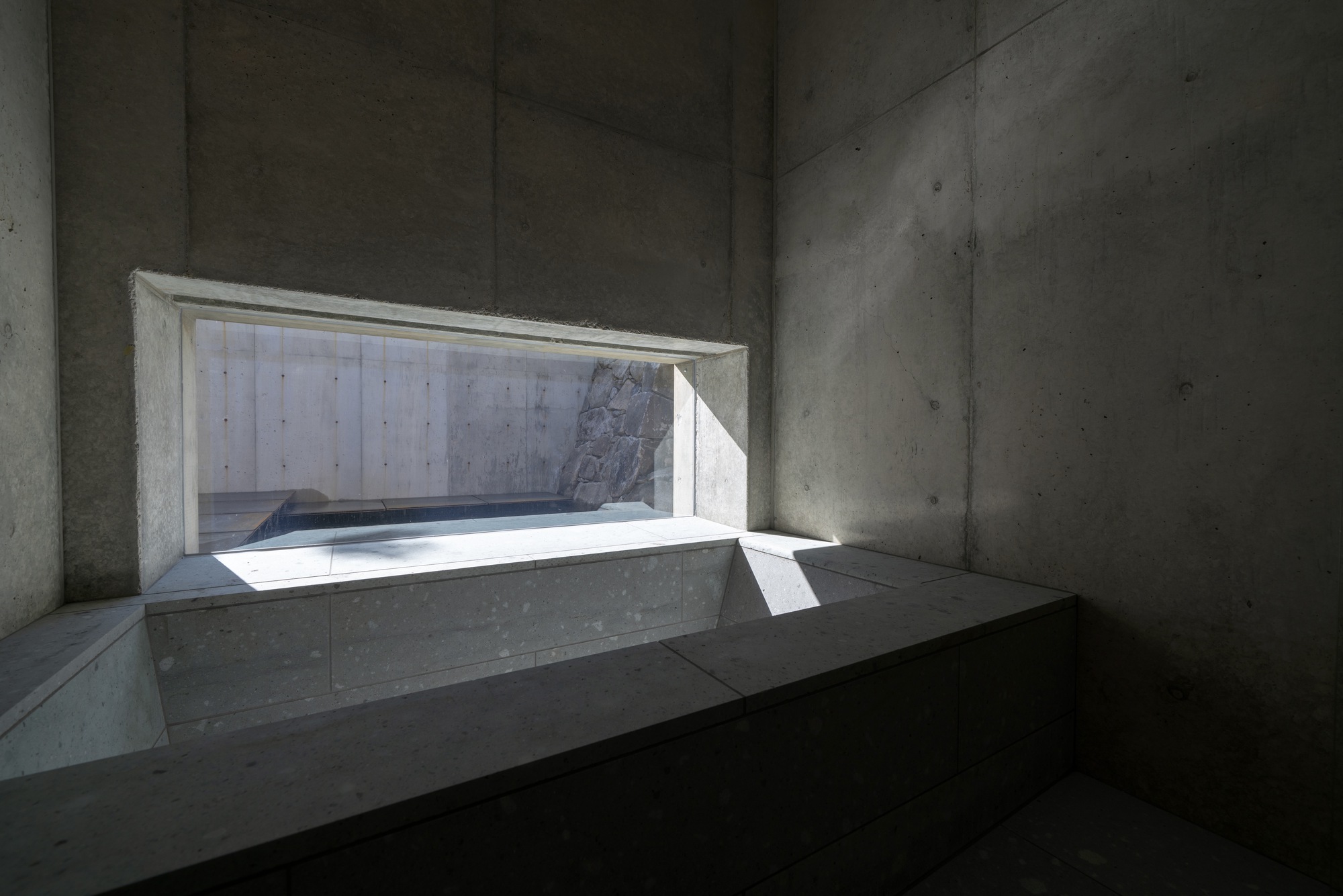 Horizontal window carved into board-formed concrete walls with bright daylight streaming through