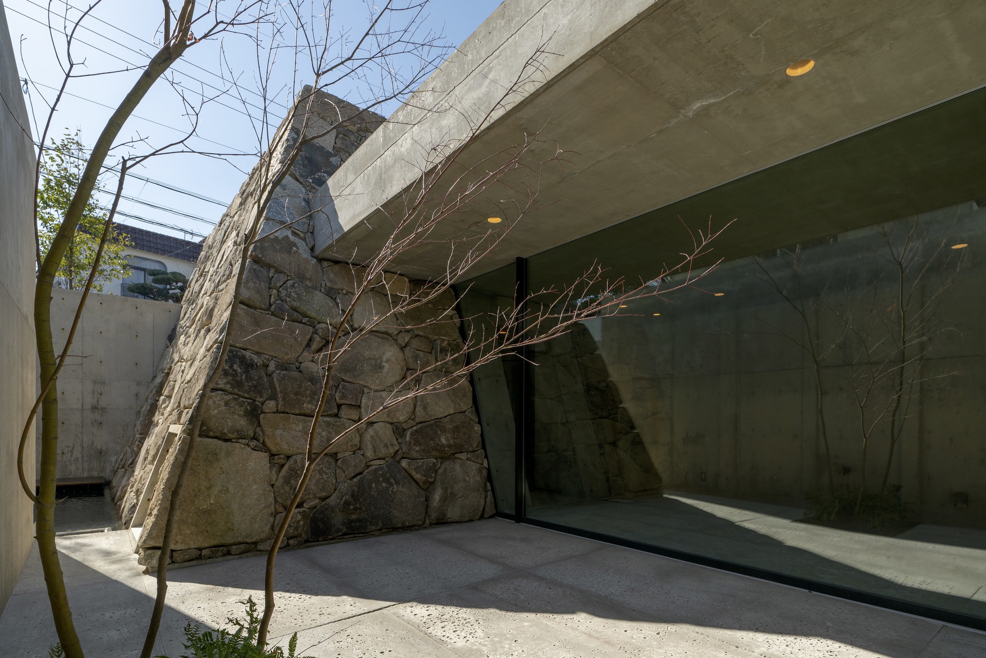 Courtyard terrace with bare tree branches against stone walls and a concrete canopy overhead
