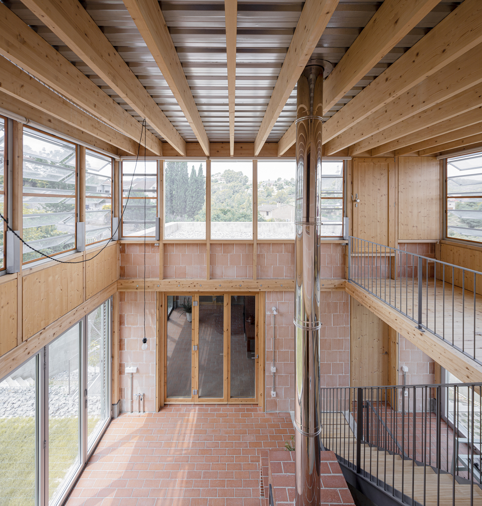 Upper-level interior view showing timber joists, clerestory windows, and steel railings overlooking the central brick floor
