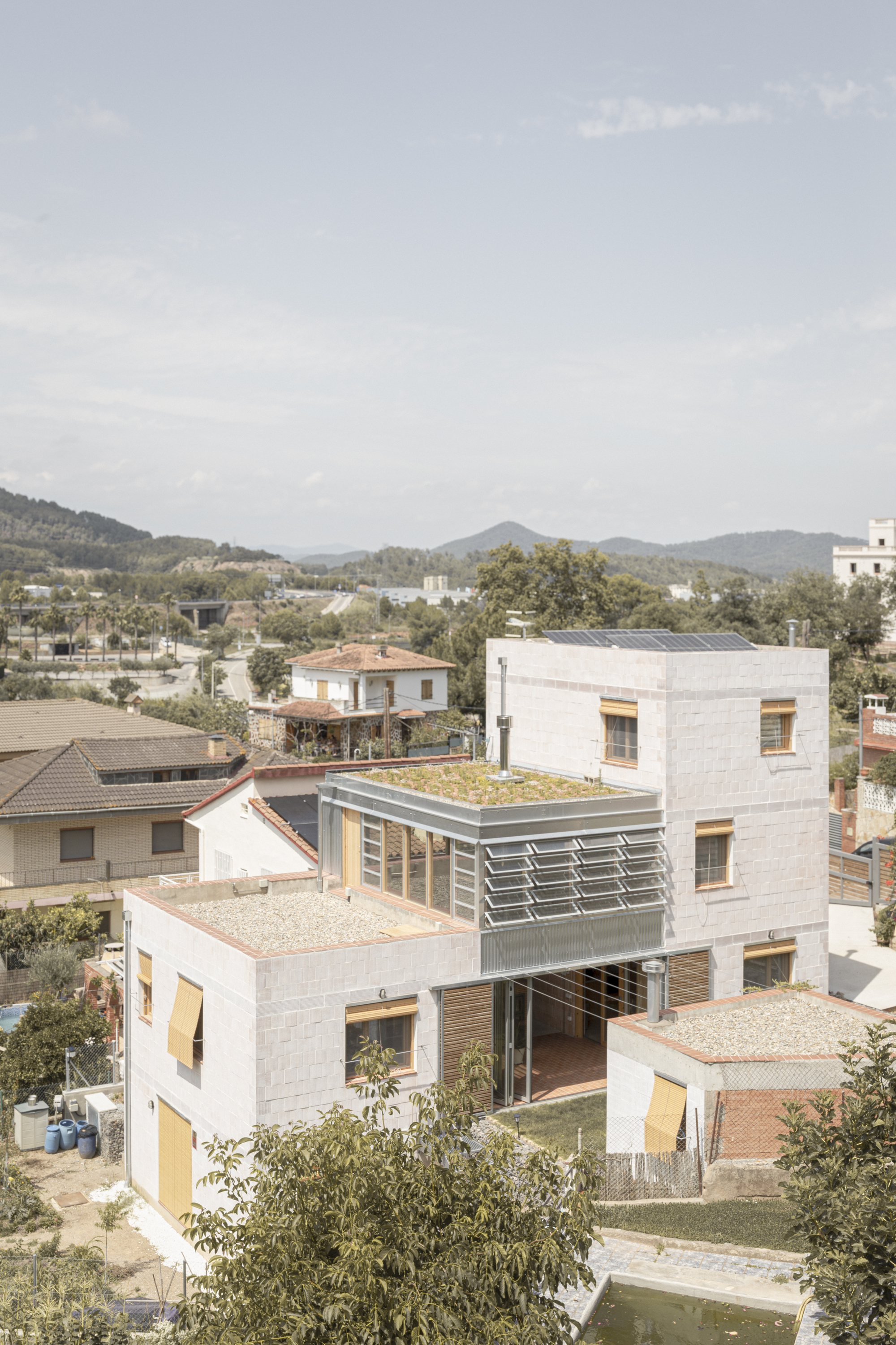 Elevated view of stacked masonry volumes with green roofs and timber louvres against distant hills