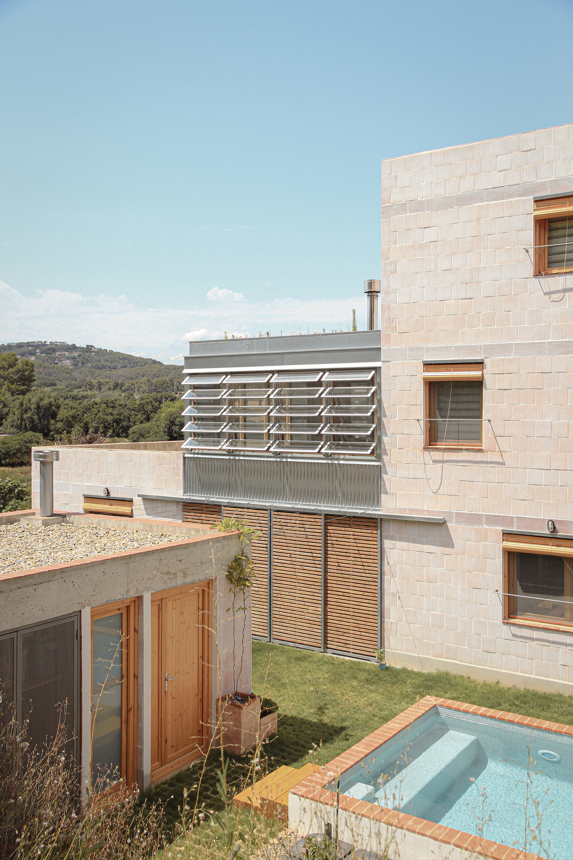 Courtyard view showing terraced volumes with block masonry walls, timber shutters, and a small pool