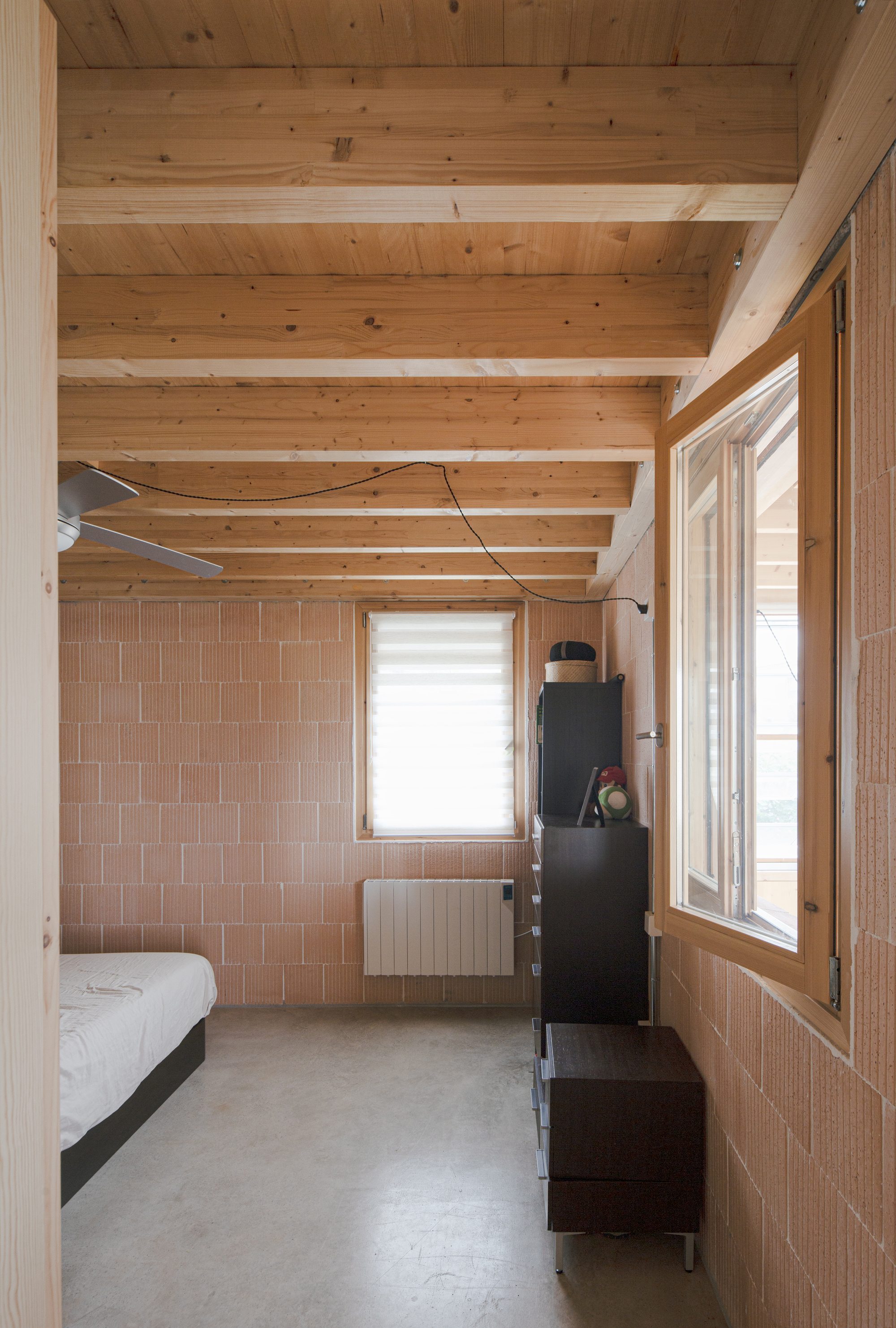 Bedroom with exposed timber beams, terracotta tile wall panels, and polished concrete floor