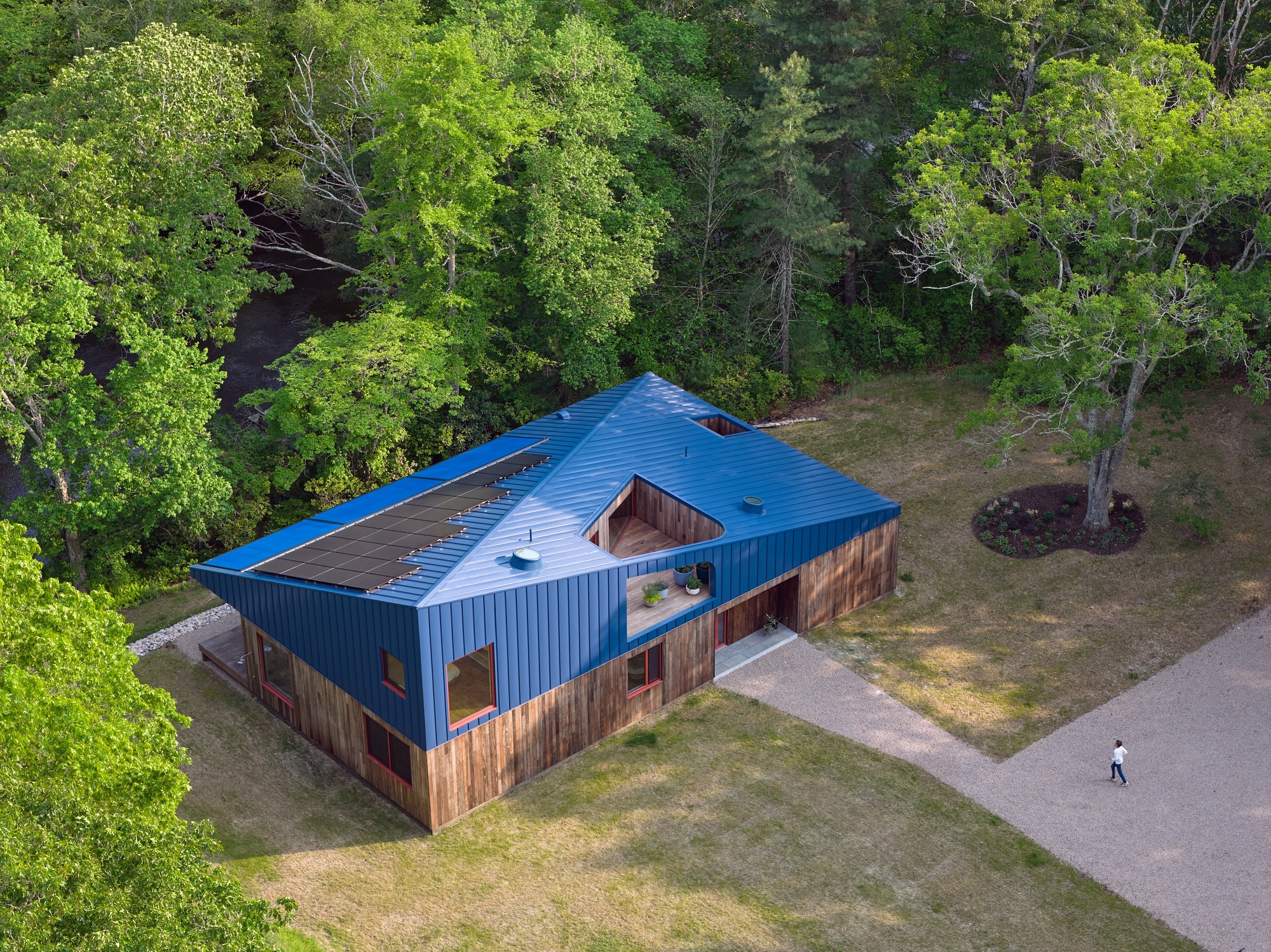 Aerial view of the blue corrugated metal roof with central skylight and weathered timber walls surrounded by forest