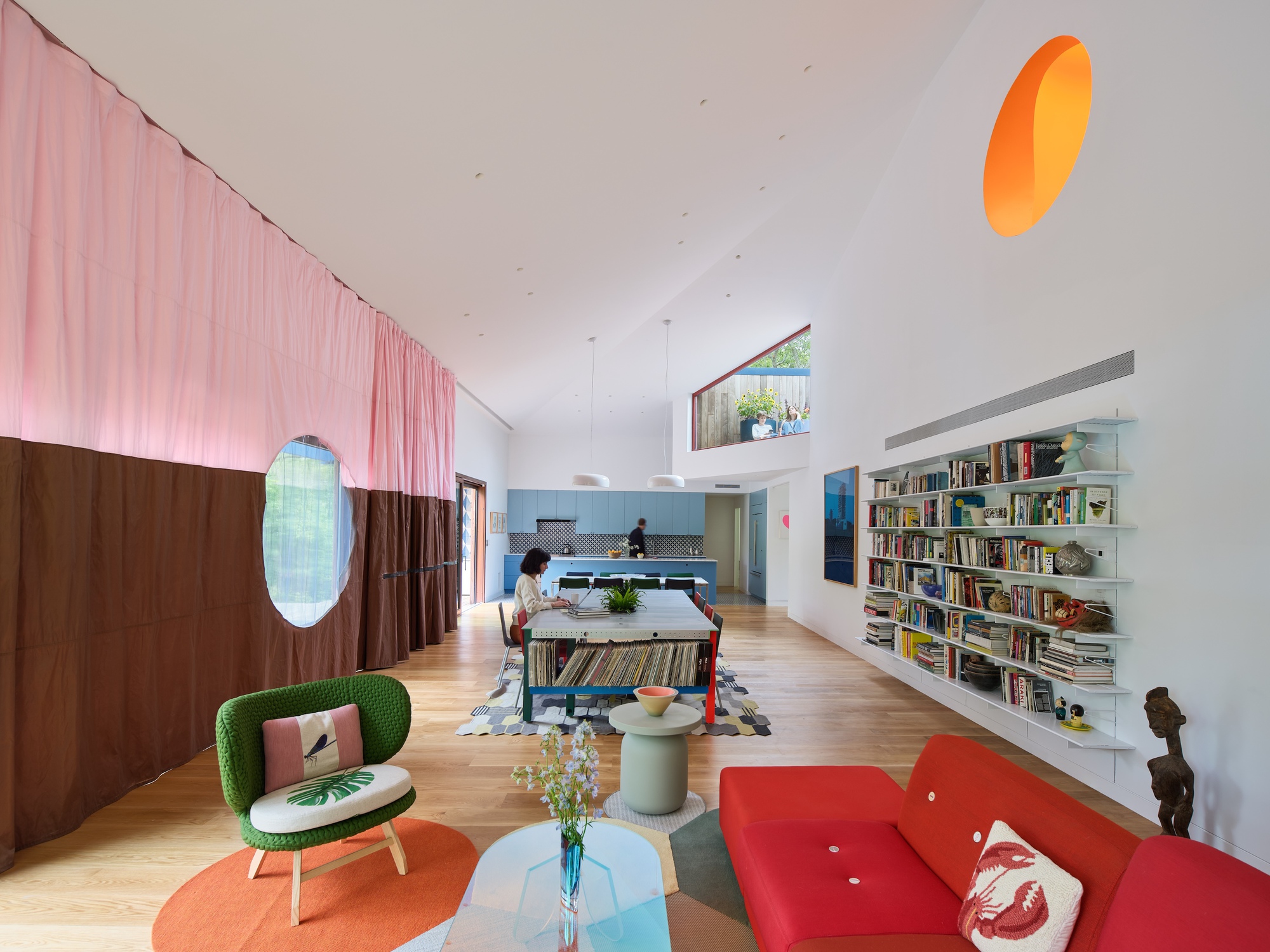 Living area with pink fabric divider, circular openings, oak flooring, and built-in bookshelves under vaulted ceiling