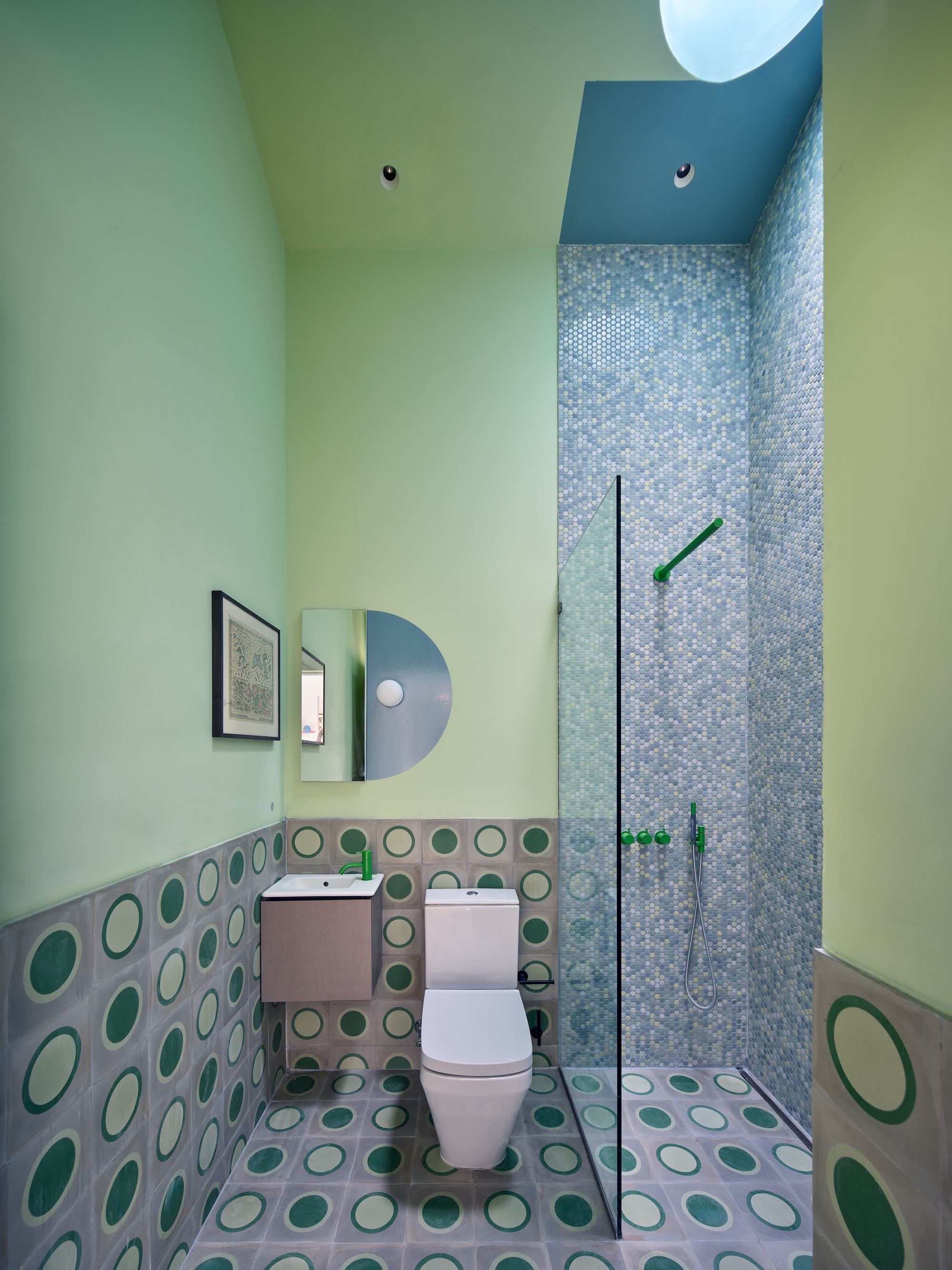 Bathroom with circular patterned floor and wall tiles, glass shower screen, and pale green walls