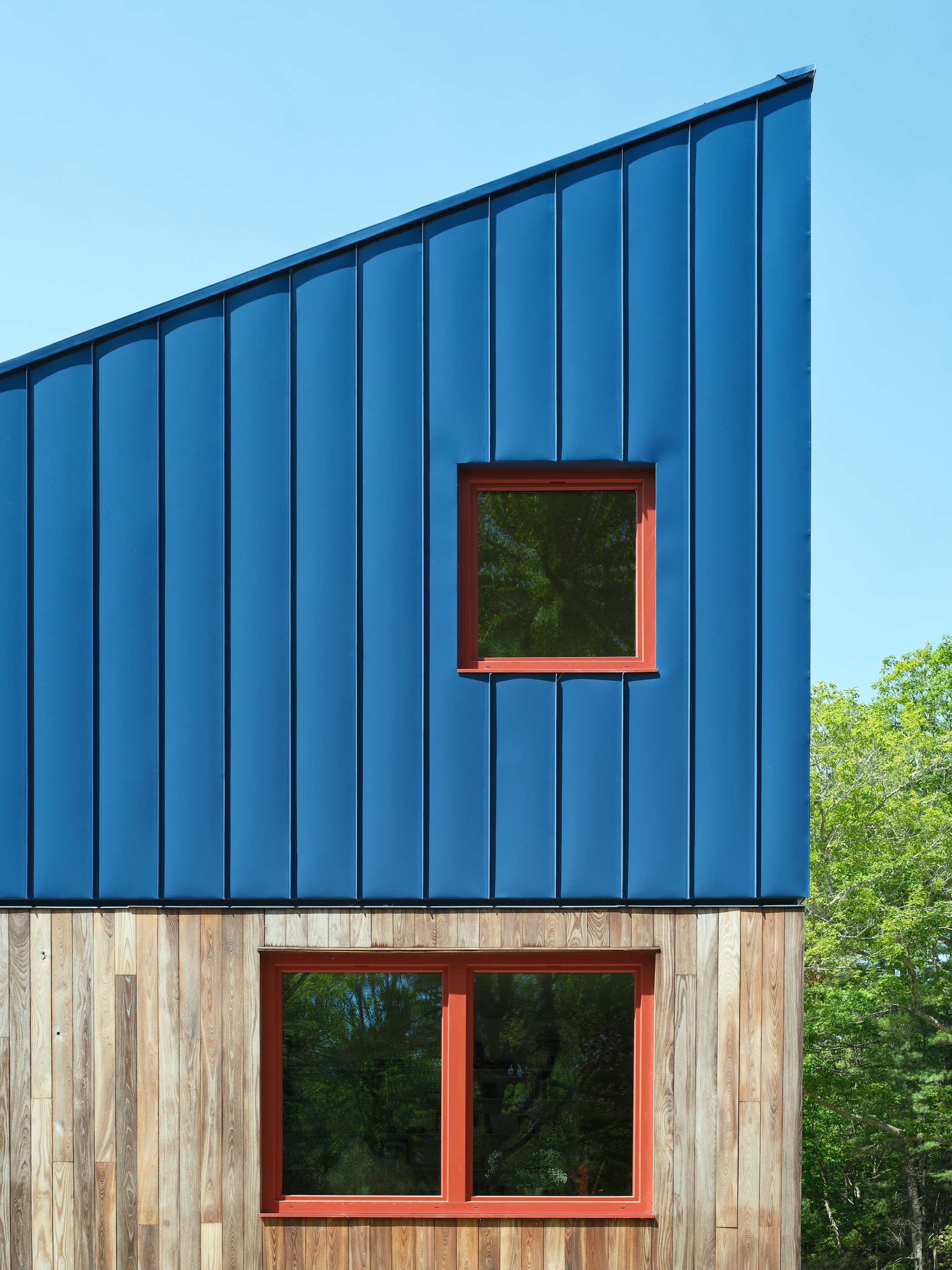 Two-story facade showing blue metal cladding above weathered timber with stacked windows framed in red