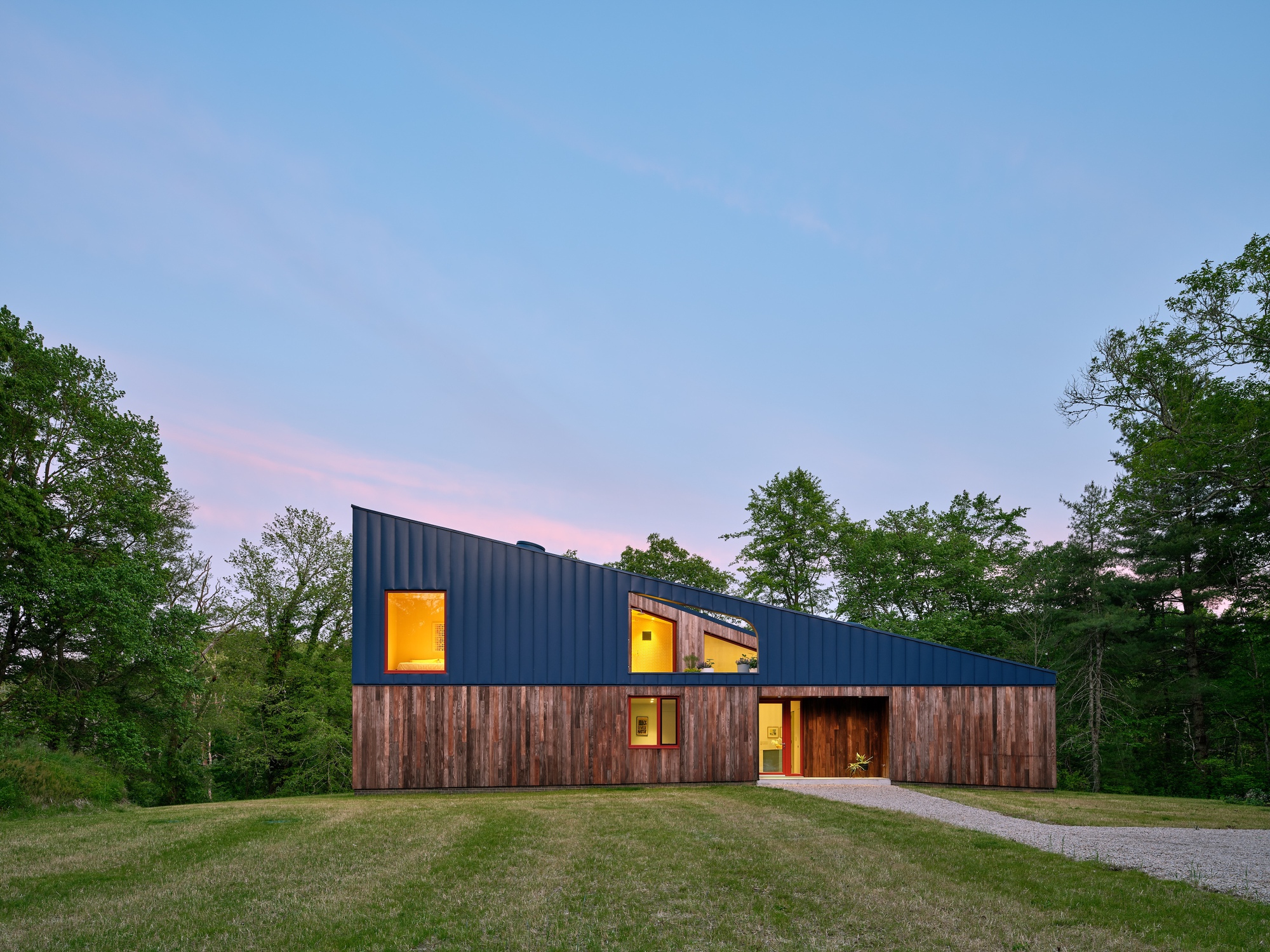 Timber and blue metal facade with illuminated windows at dusk against a pink sky