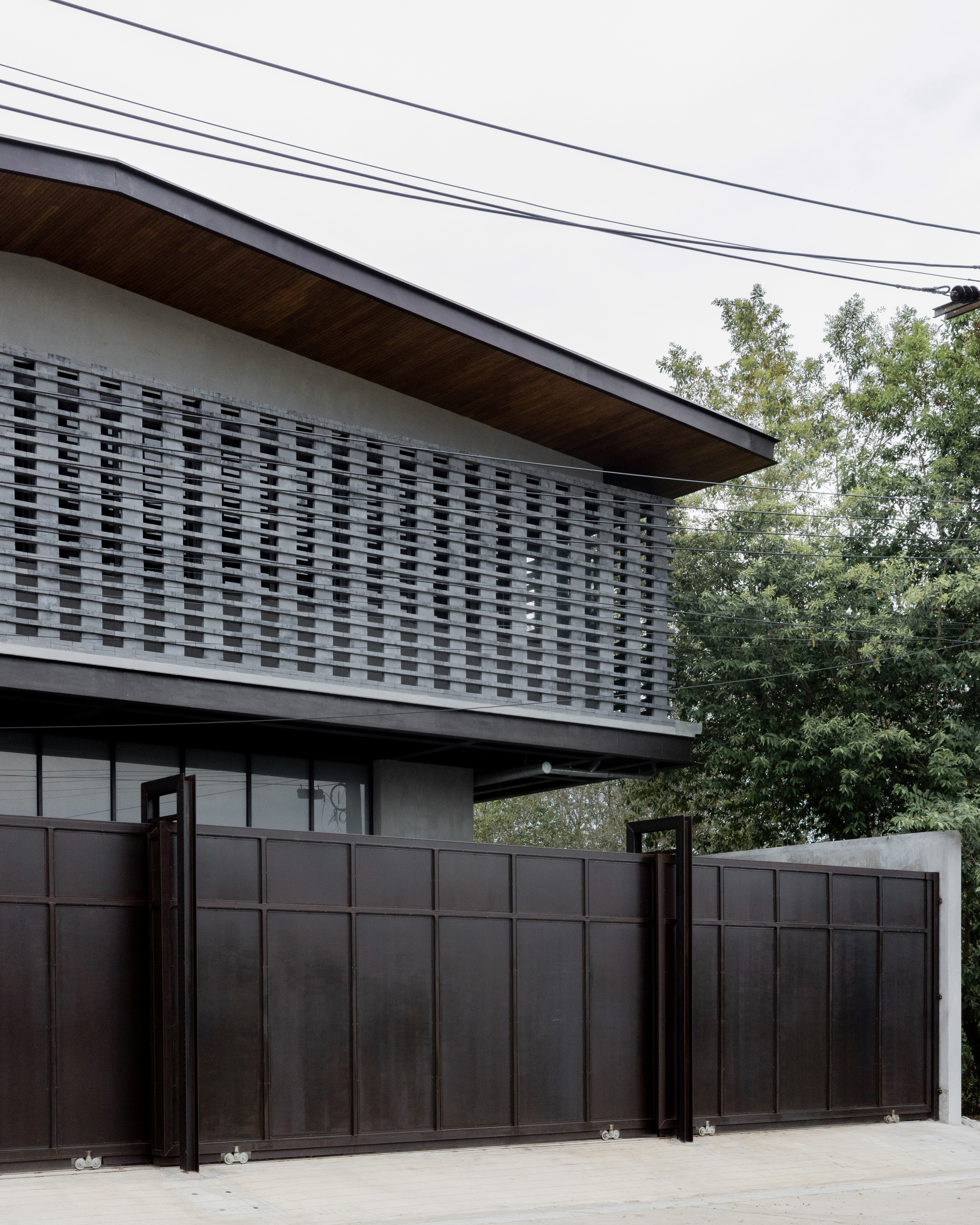 Detail of the woven brick screen wall above the metal gate with trees in the background