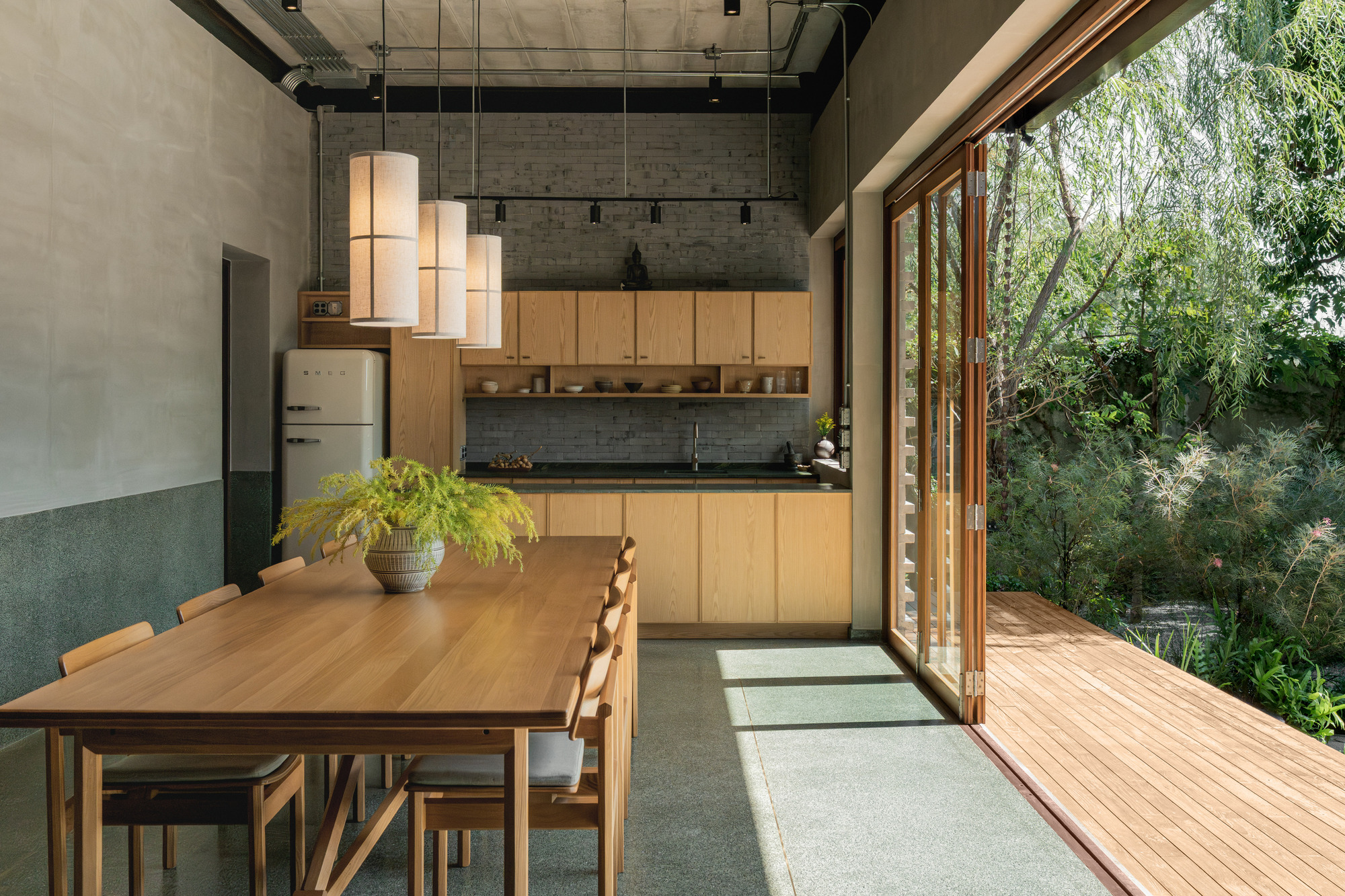 Kitchen and dining space opening onto a timber deck through floor-to-ceiling glazed doors with garden beyond
