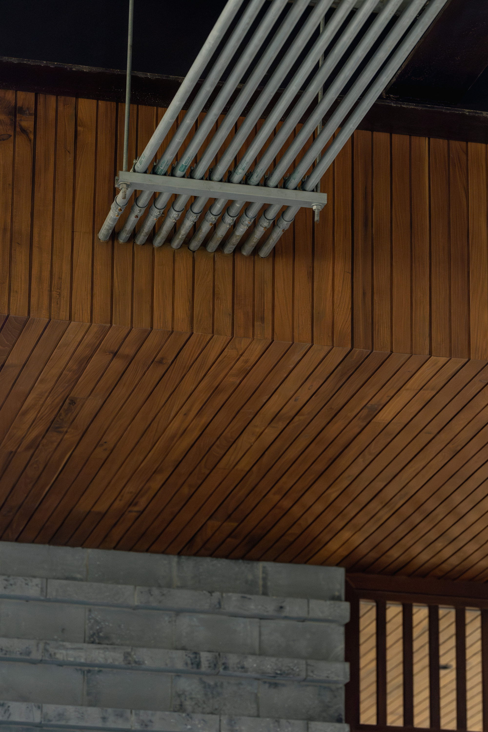 Interior ceiling with diagonal timber slat paneling meeting a skylight frame and concrete block wall