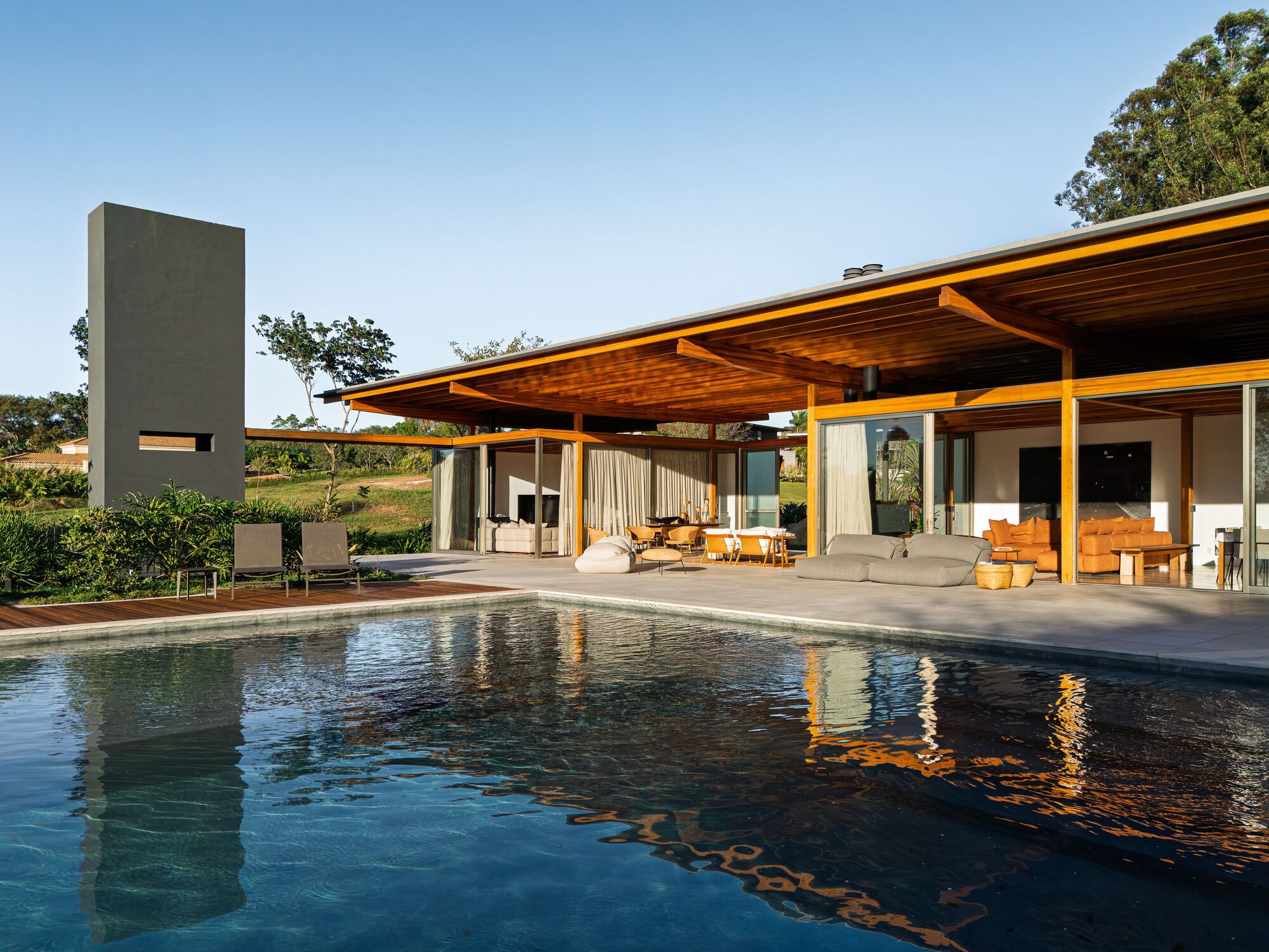 Pool terrace with reflecting water beside an open pavilion featuring exposed timber rafters and concrete chimney