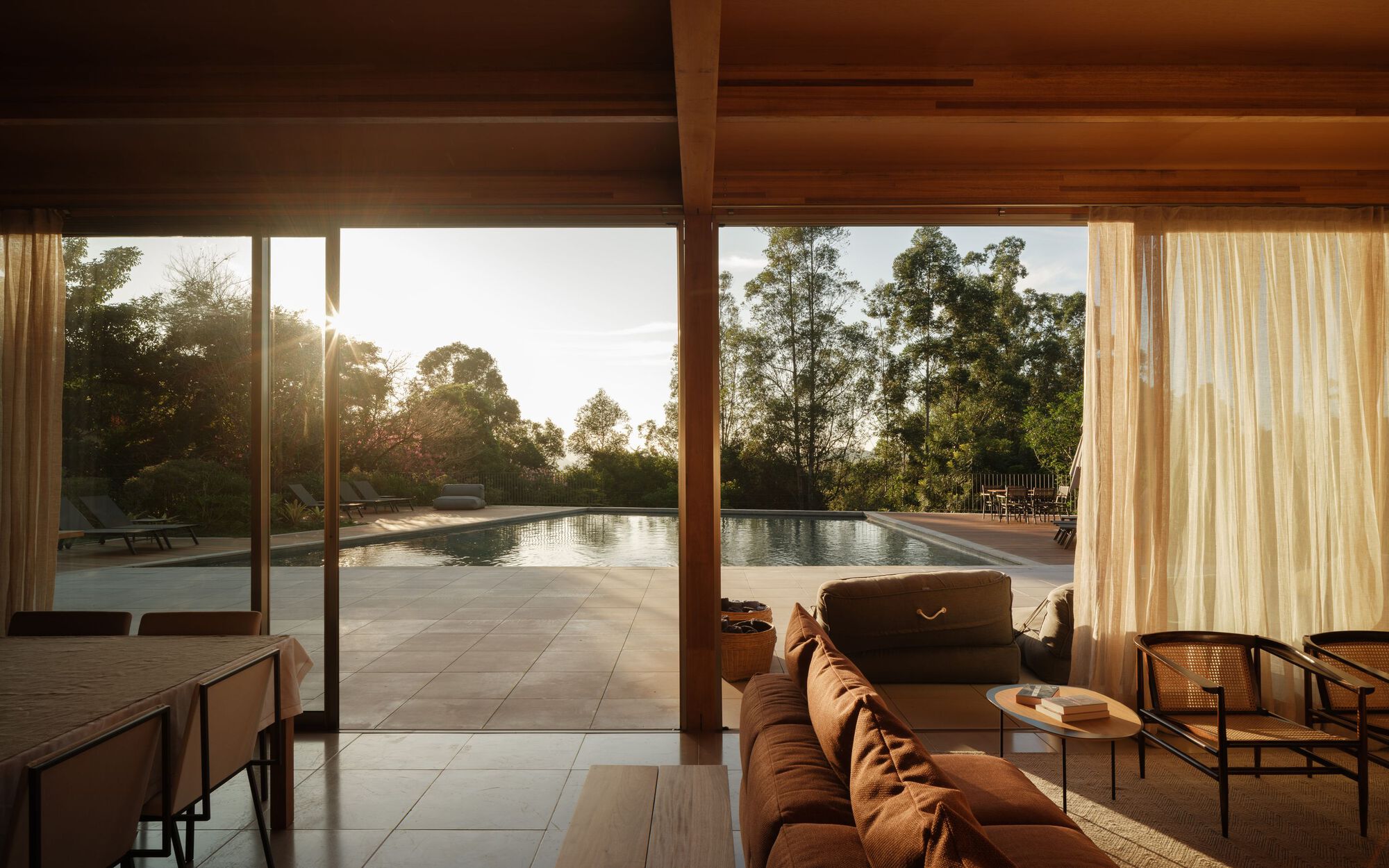 Living room with timber ceiling overhang framing view of lap pool and trees at sunset
