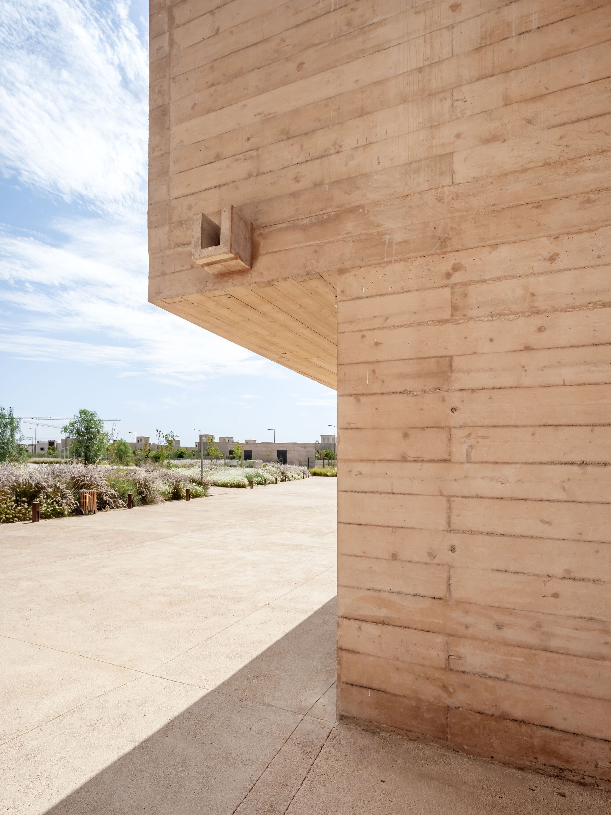 Corner detail of cantilevered rammed earth volume with small cubic birdhouse opening under clouds