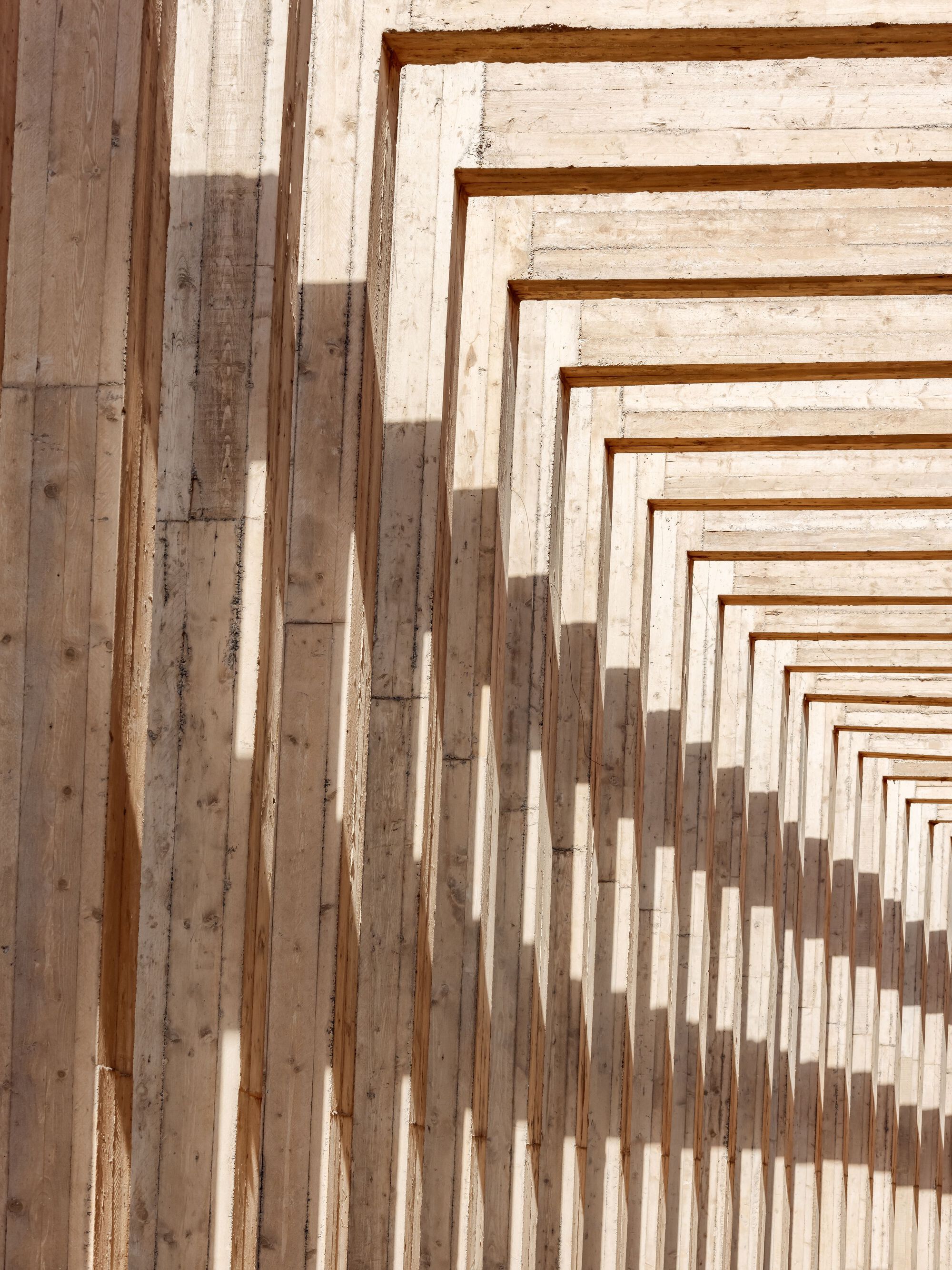 Stepped timber beams forming a rhythmic pergola structure casting shadows in bright sunlight