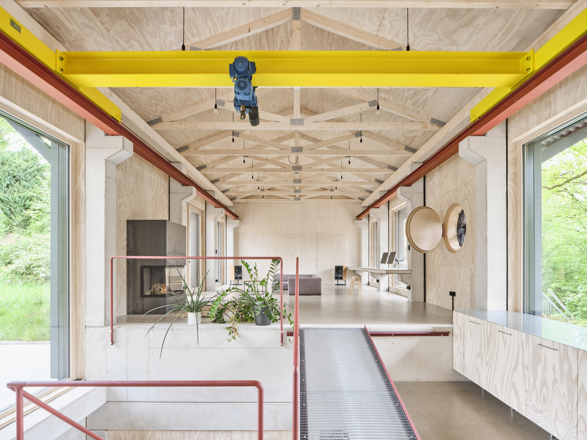 Interior view showing exposed timber truss ceiling with yellow overhead crane beam and plywood walls framing large windows
